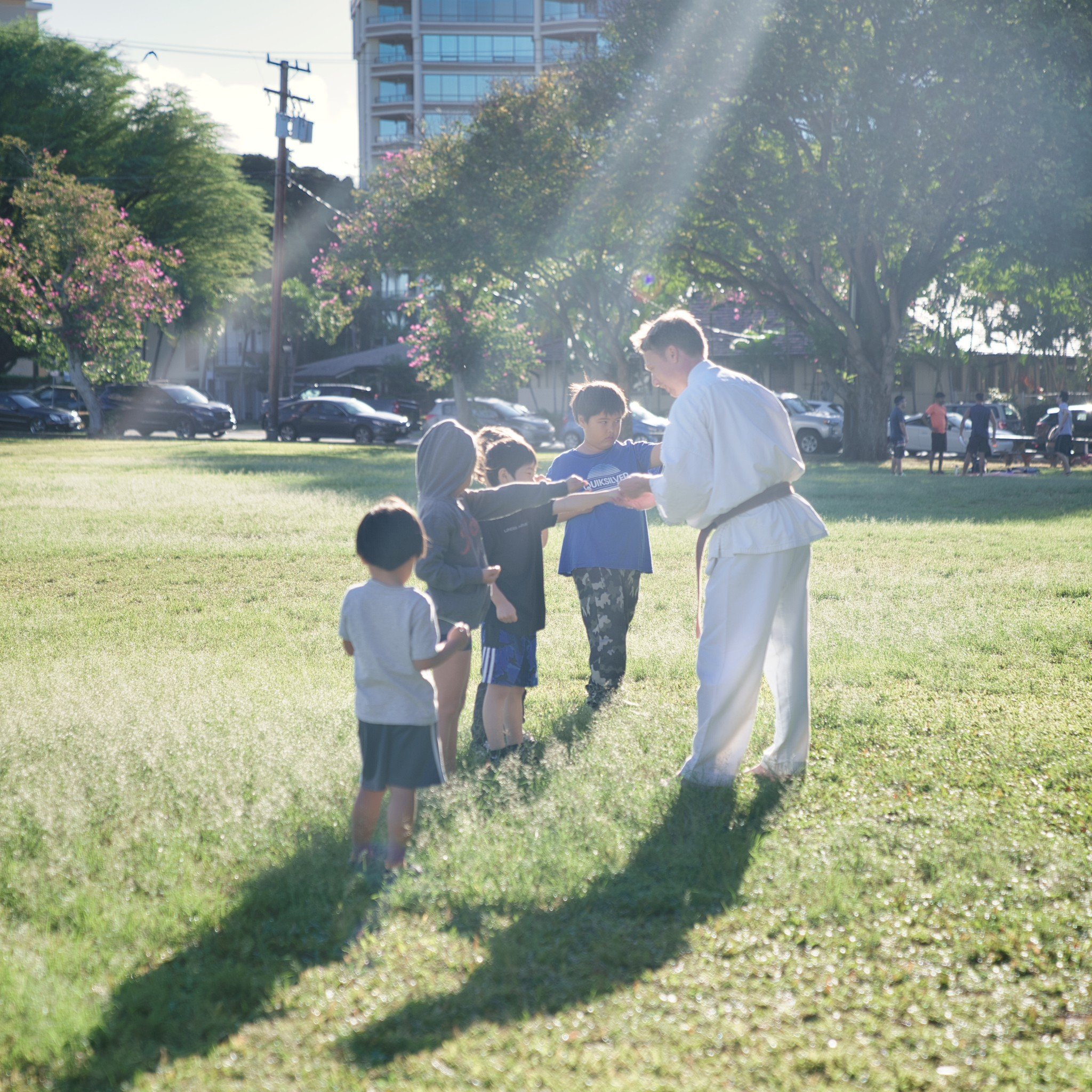 Martial arts instructor demonstrating techniques to children outdoors in a park during daytime.