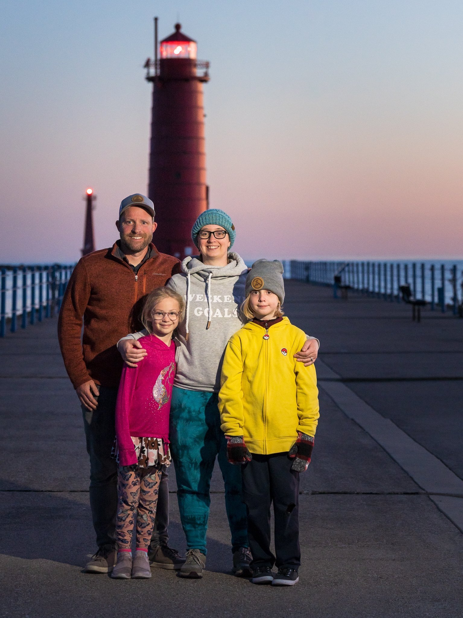 Family of 4 at sunset, standing in front of a lighthouse.
