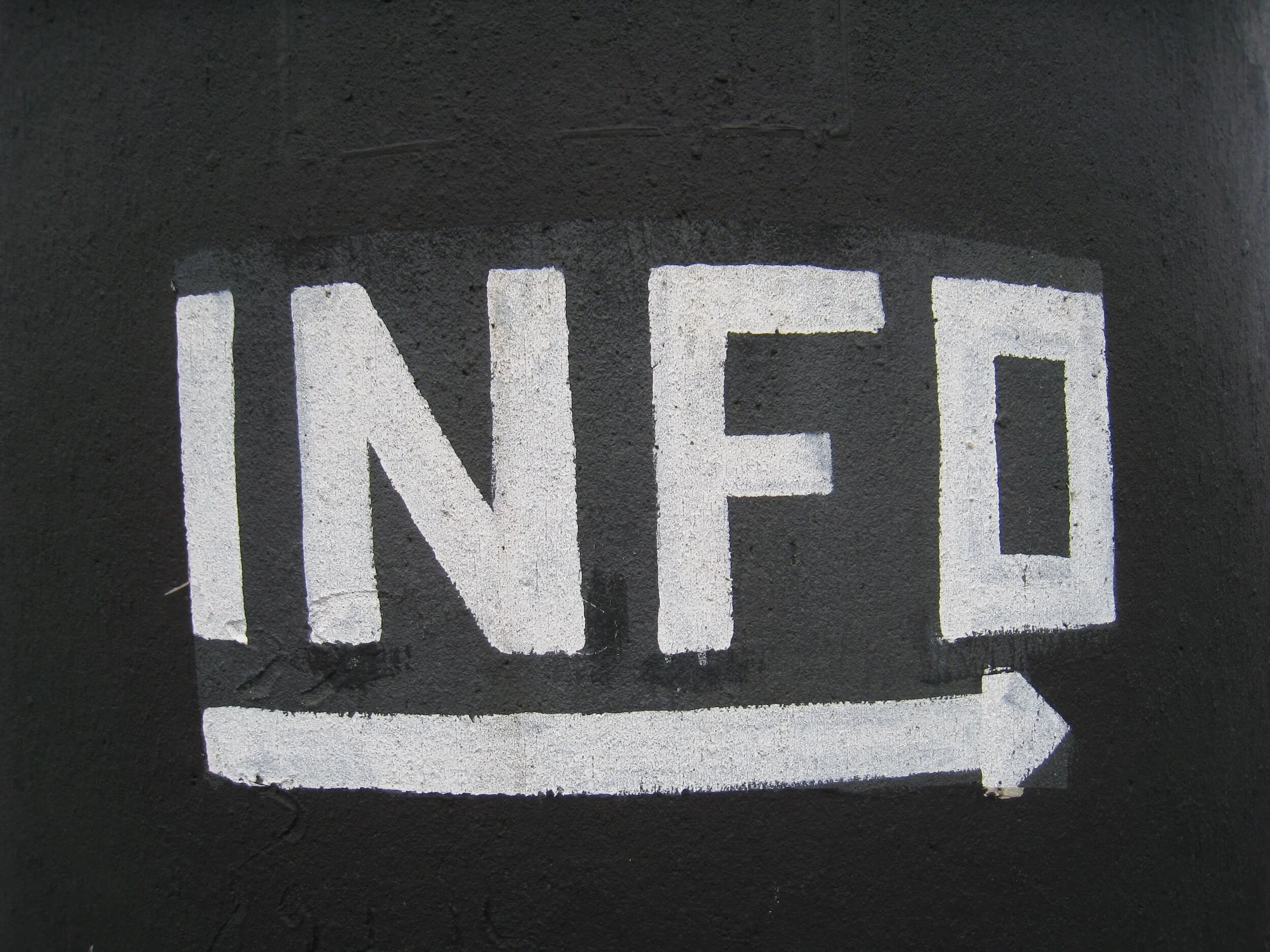 "INFO" painted in white on black surface with arrow pointing right