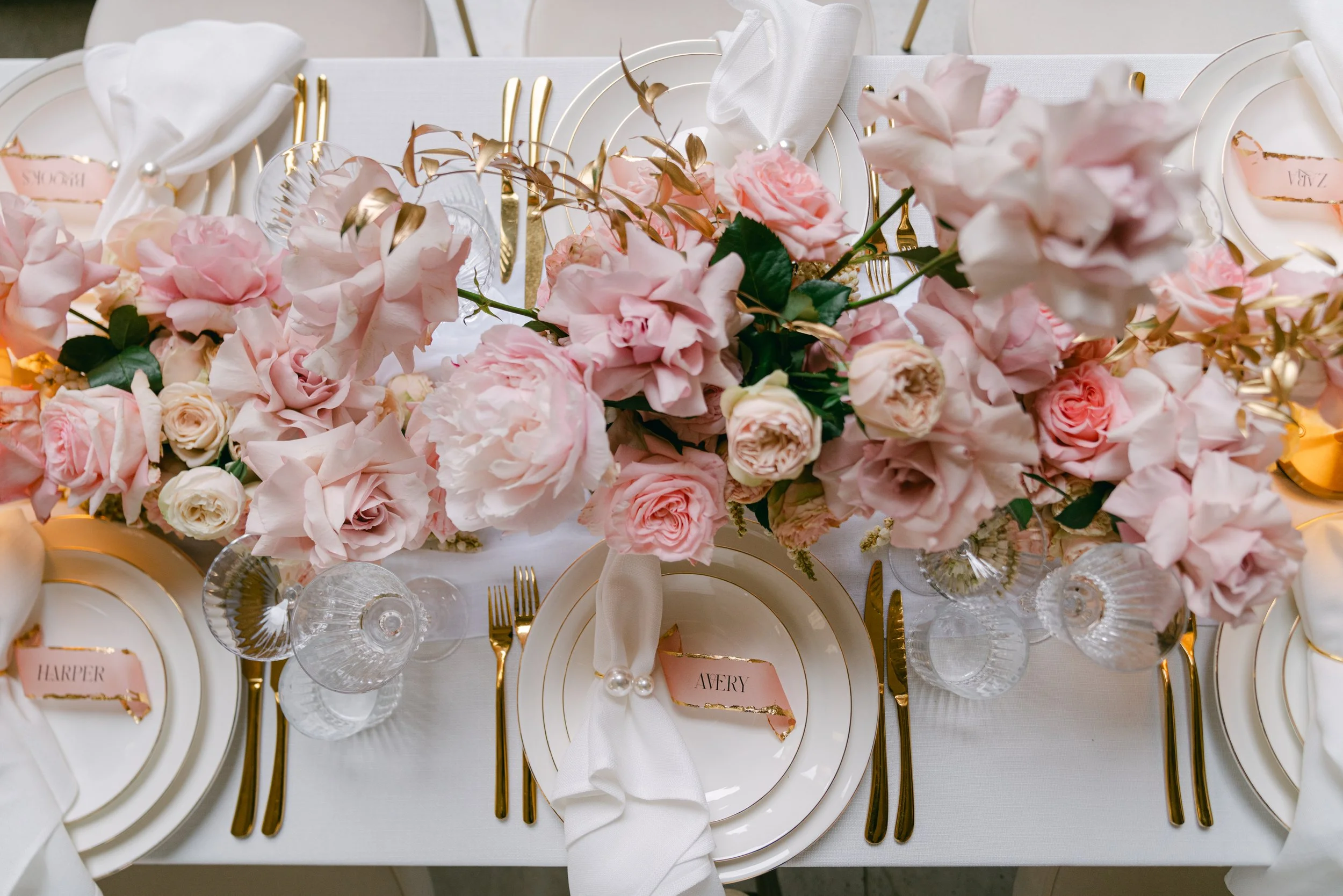 Elegant table setting with pink and white flowers, gold cutlery, and white plates with gold rims at a wedding reception.