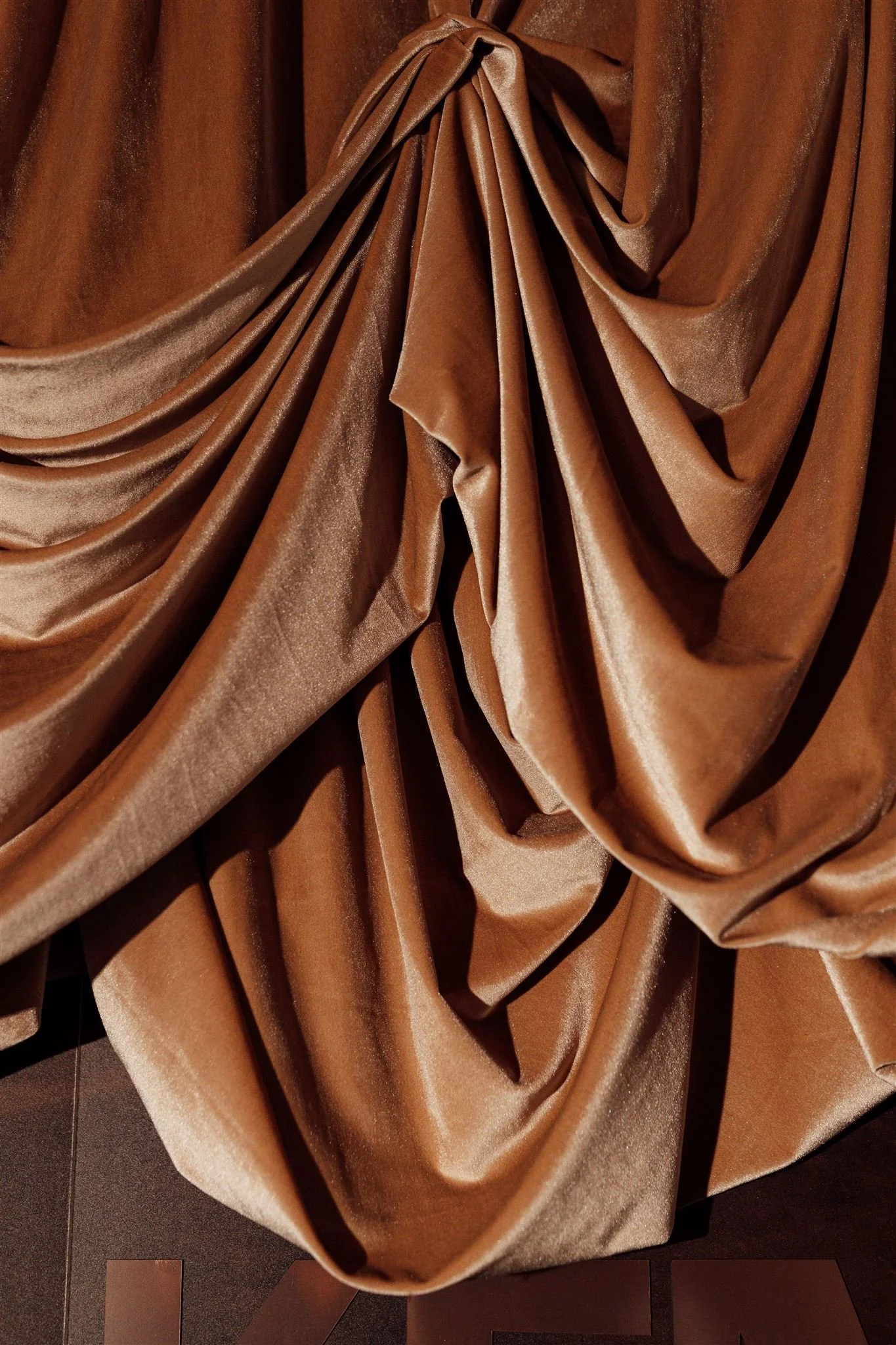 Close-up of shiny, brown, velvety fabric gathered and draped with soft folds.