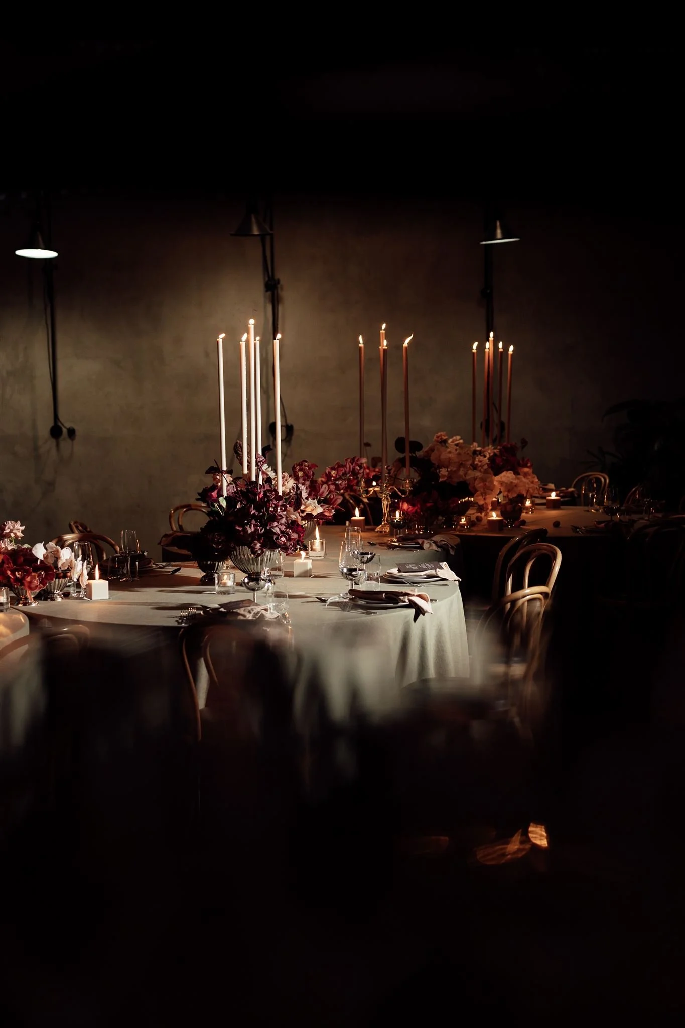 A dimly lit dining table decorated with flower arrangements and tall candles in a sophisticated setting.
