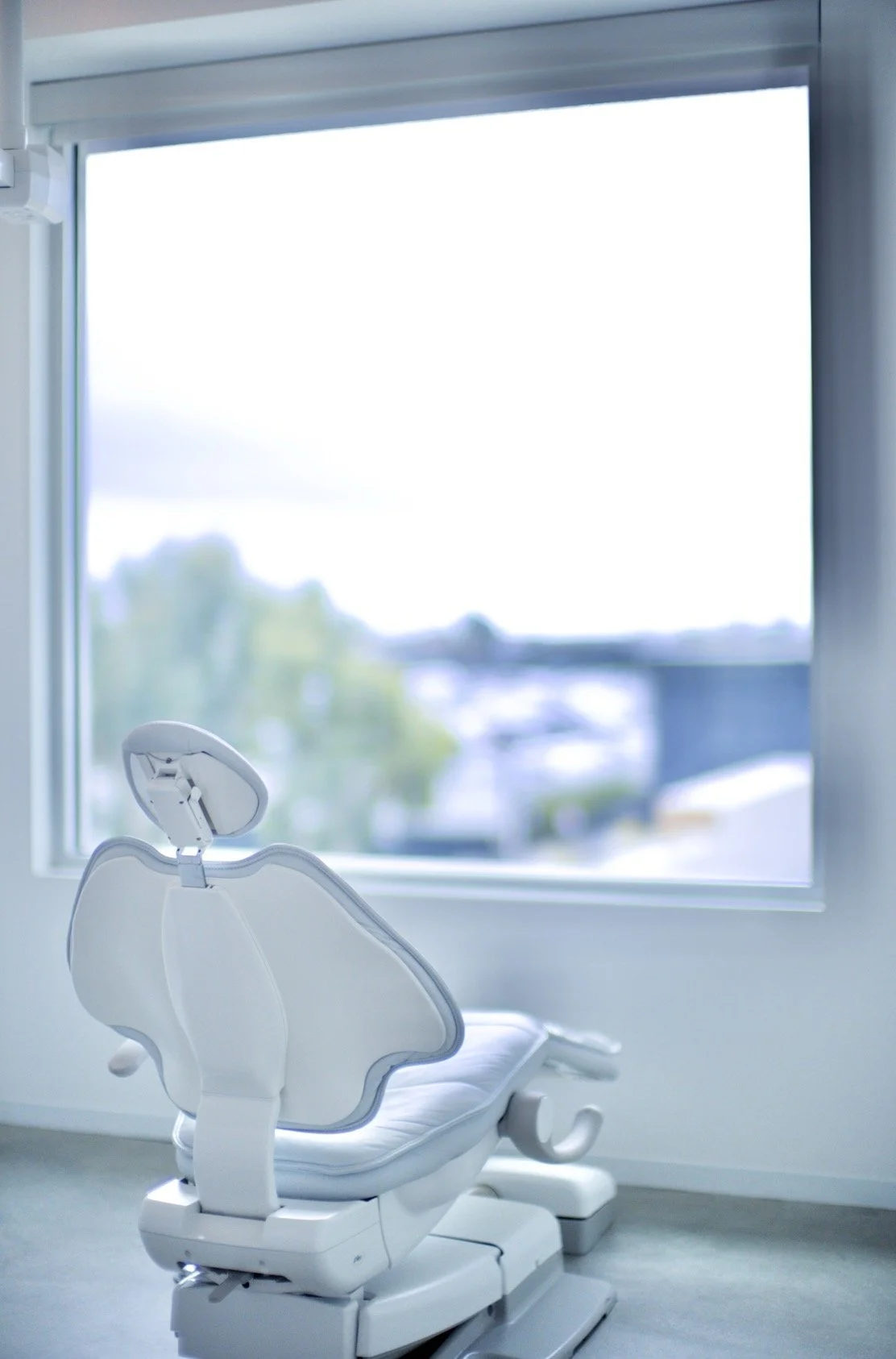 Dental chair in a room with a large window showing a blurred outdoor landscape.