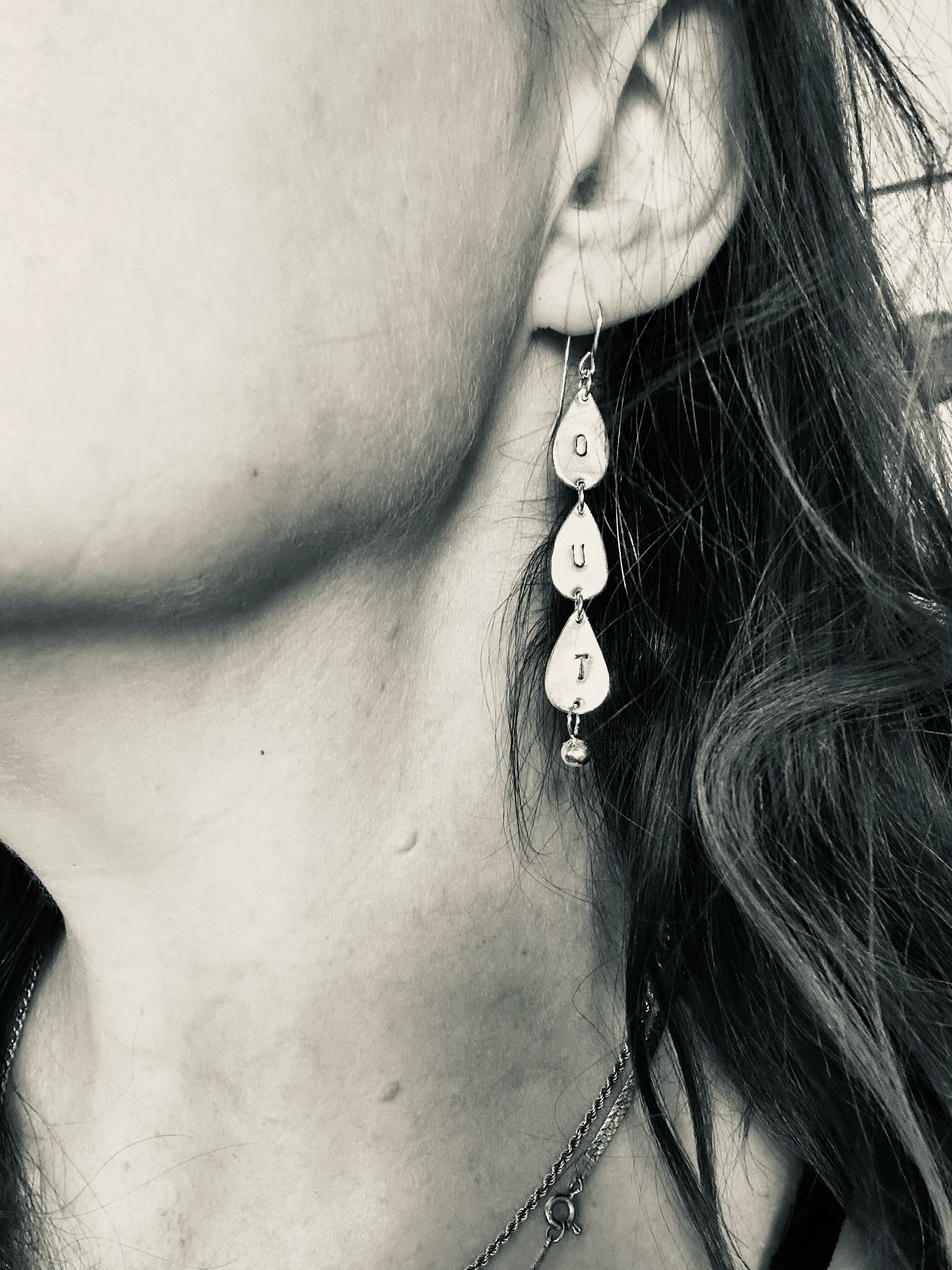 The artist posing wearing the earring that says OUT in their right ear. They have white skin and brown hair and the photo is in black and white