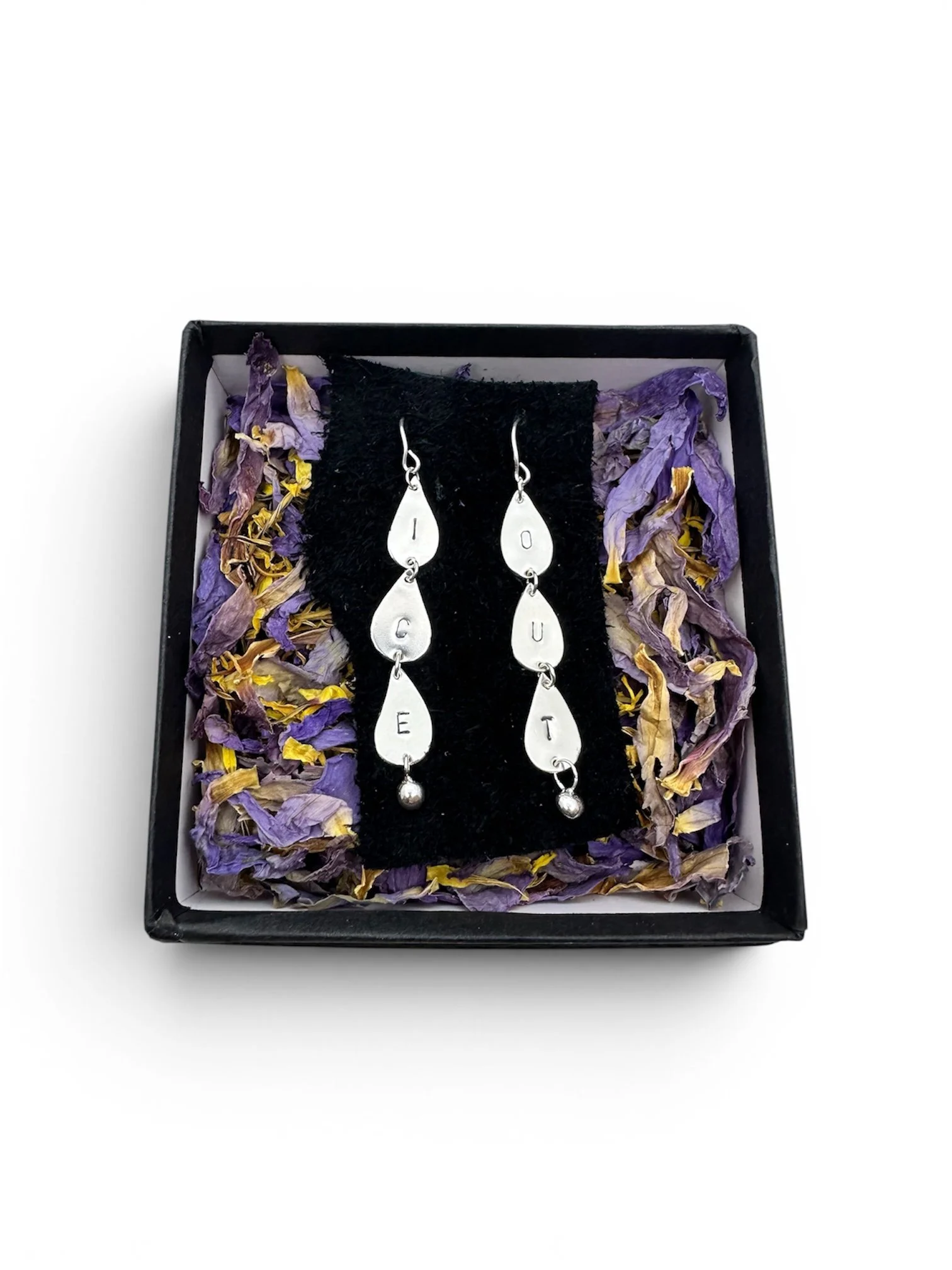 The same sterling silver ICE OUT droplet earrings as the last photo, nestled in a black square box in a bed of beautiful blue lotus petals.