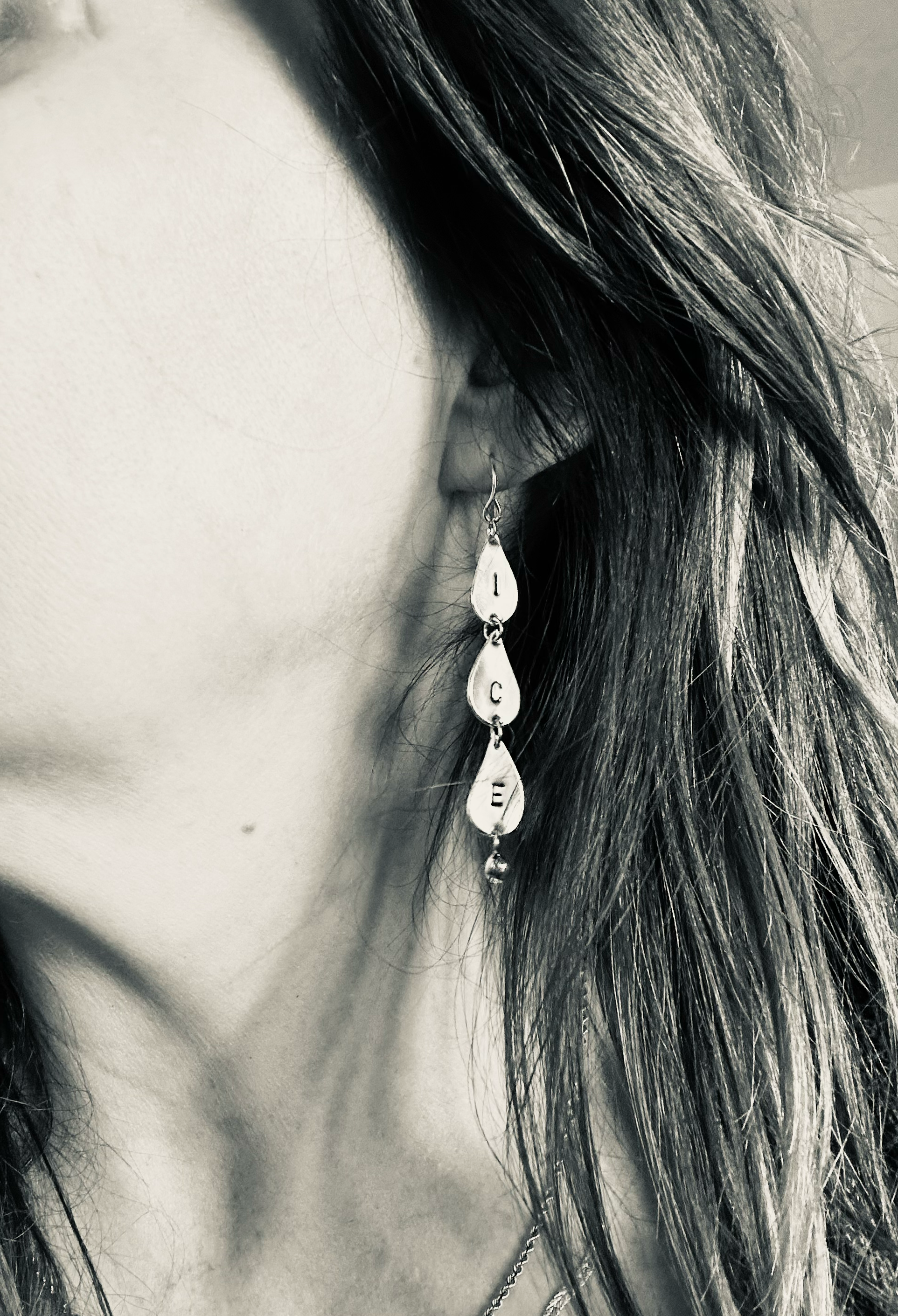 The artist posing wearing the earring that says ICE in their left ear. They have white skin and brown hair and the photo is in black and white