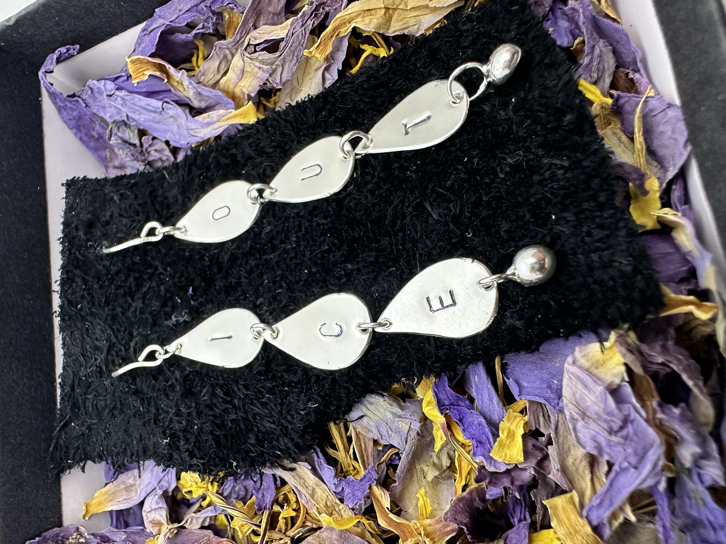 A zoomed in closeup of the same sterling silver ICE OUT droplet earrings, nestled in a bed of beautiful blue lotus petals.