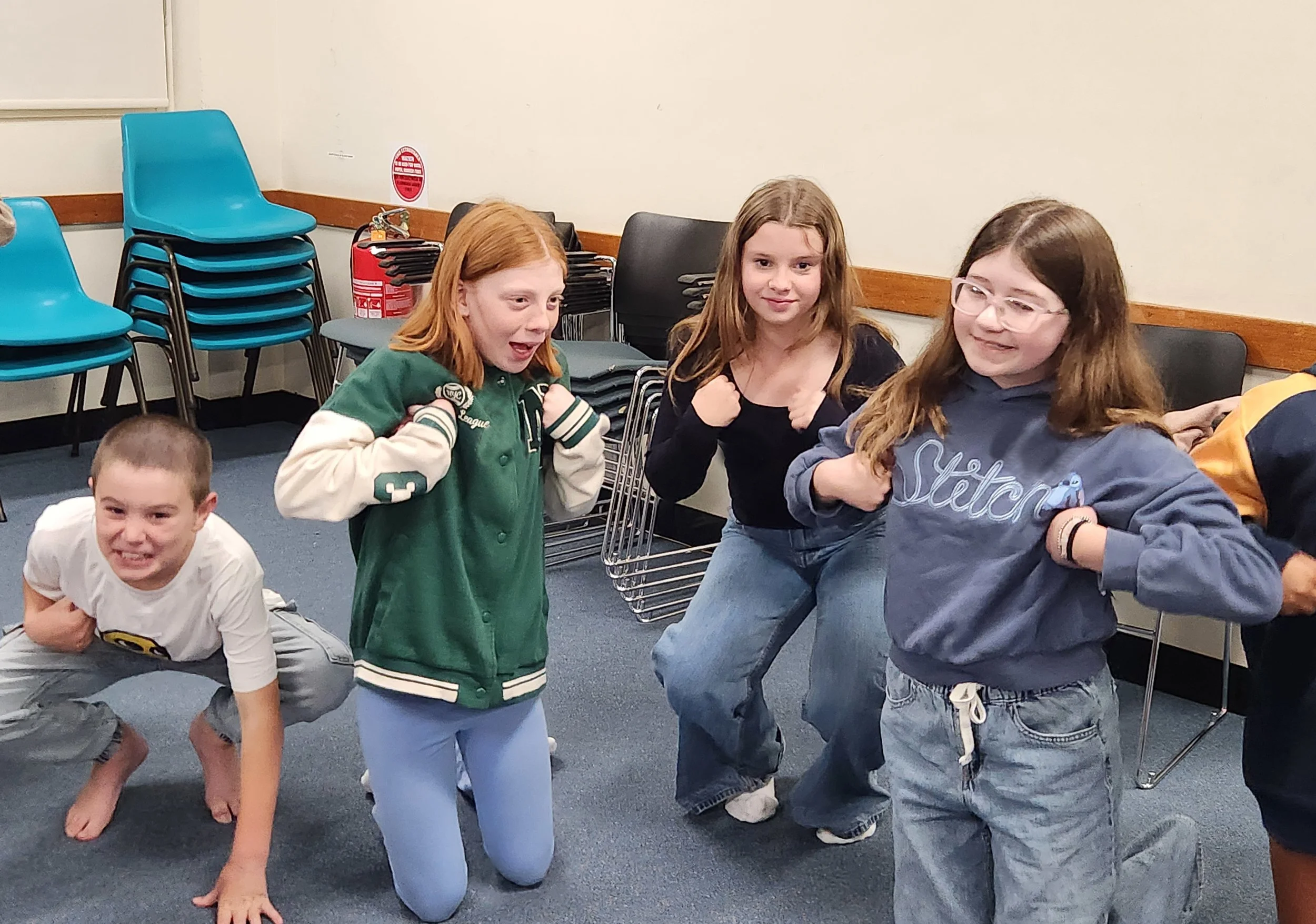 A group of children posing in a classroom, with some crouching and others standing, showing excitement and confidence.