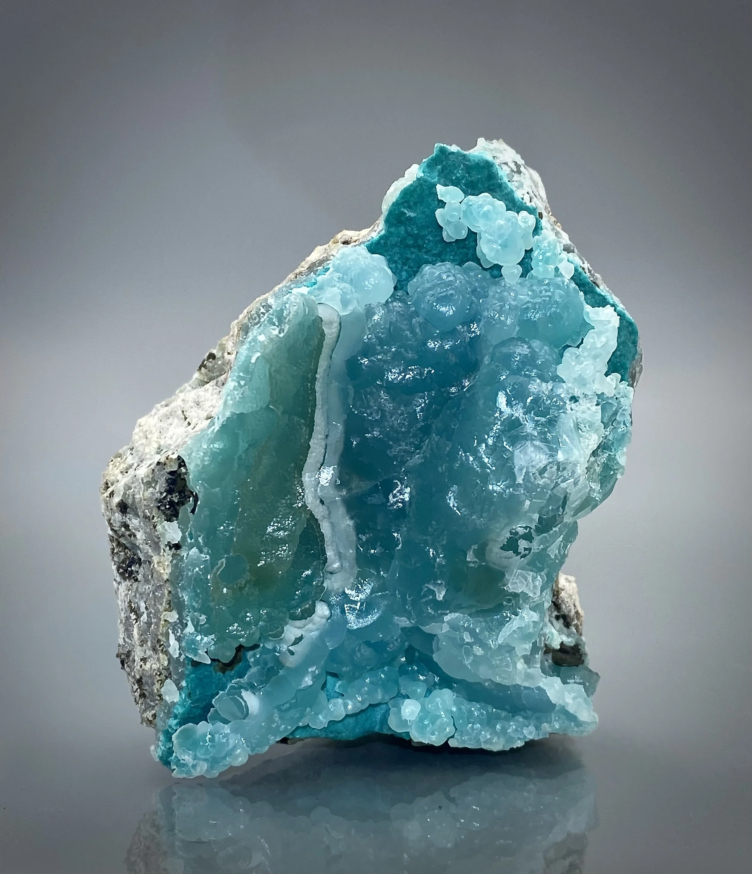 A blue mineral or crystal specimen with a rough, uneven surface and crystalline formations, set against a plain gray background.