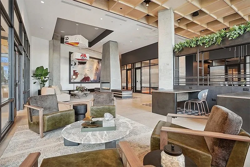 Modern hotel lobby with seating area, marble coffee table, abstract wall art, potted plant, and a lofted area with greenery.