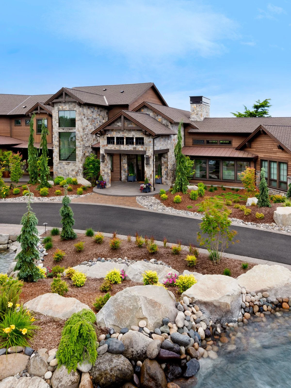 A landscaped front yard with a water feature, trees, and a modern house with stone and wood exterior, under a blue sky.