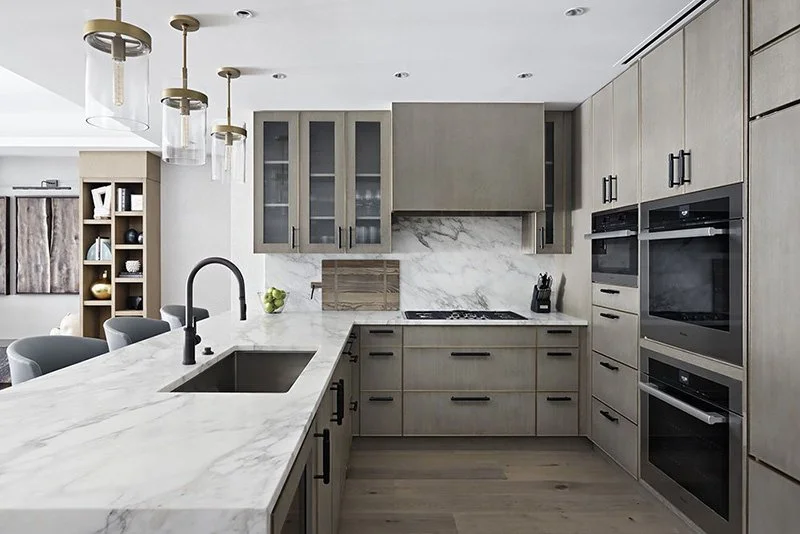 Modern kitchen with gray cabinetry, marble countertops, built-in oven, and pendant lighting.