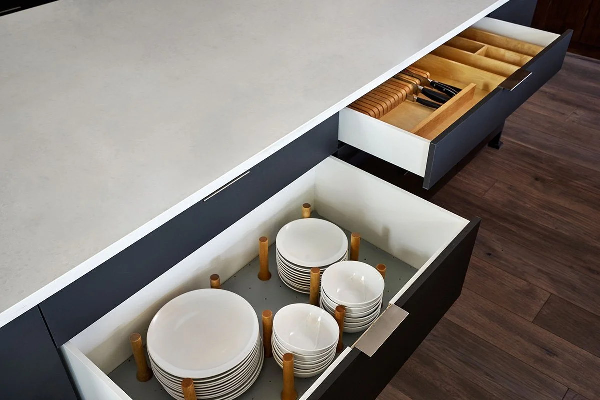 A drawer with plates and bowls held in place by adjustable pegs.