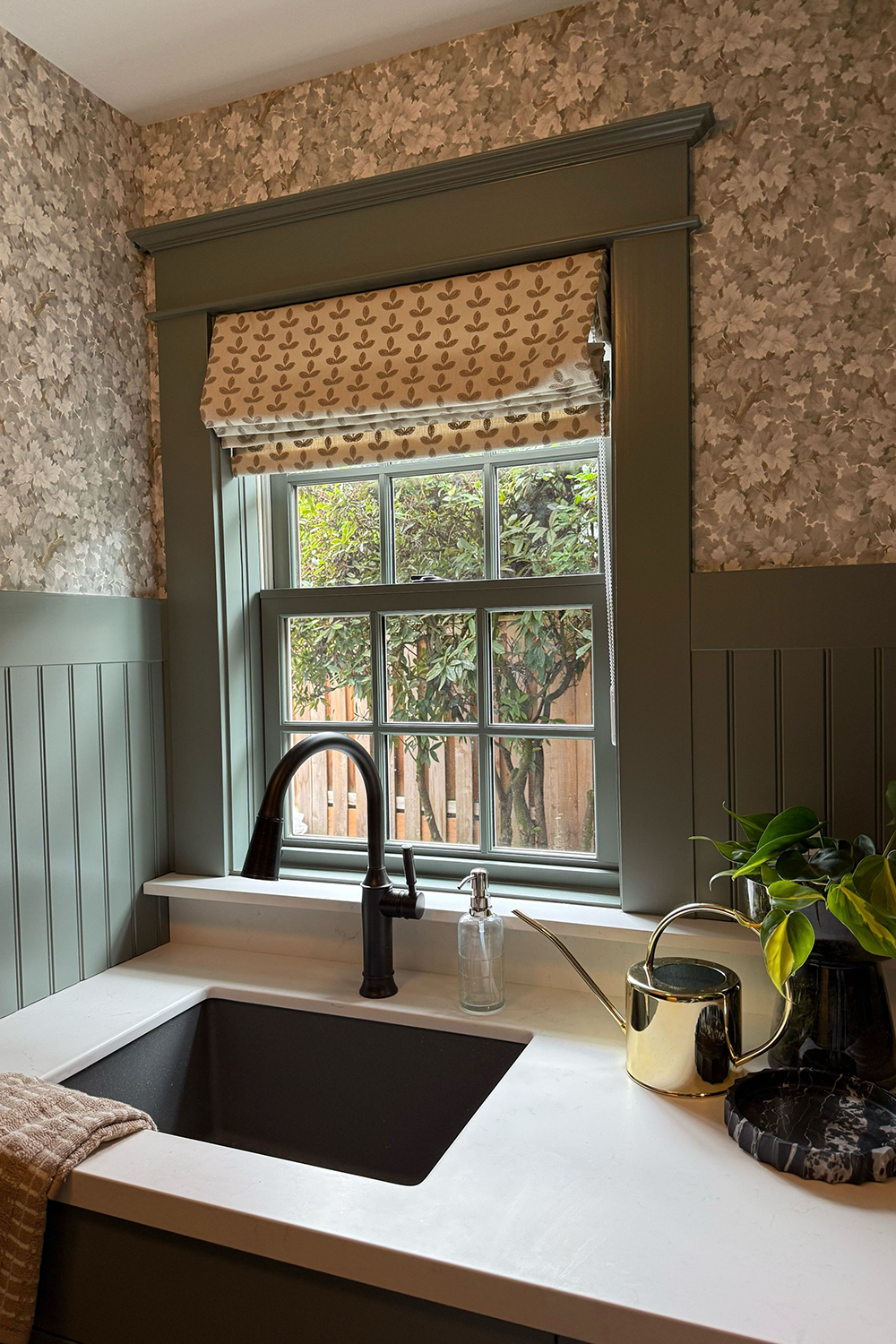 Portland laundry room after remodel, sage beadboard wainscoting, botanical wallpaper, matte black sink and custom Roman shade, by Studio Garrison.