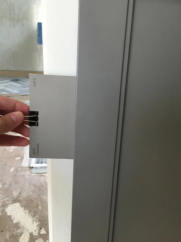 A color swatch being compared to a cabinet sample by an interior designer.