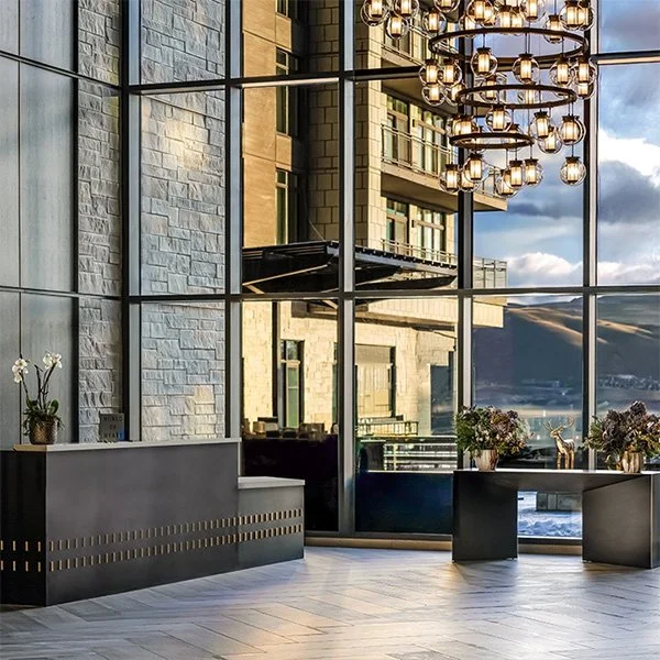 A tall ceilinged lobby with large windows and chandelier. 