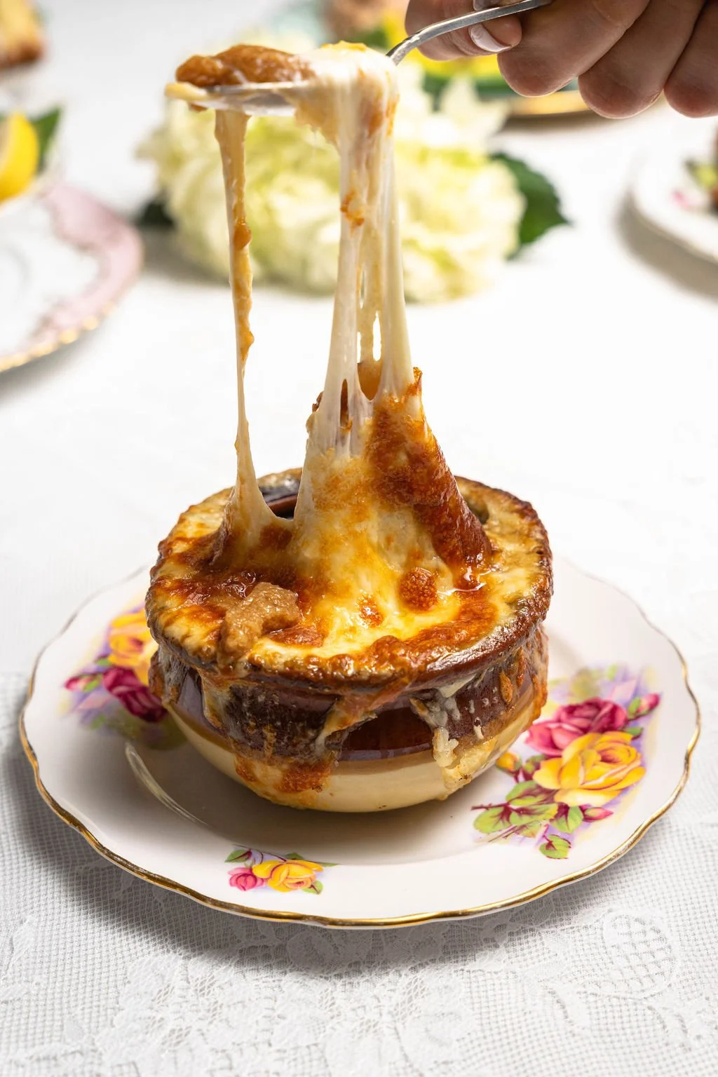 French onion soup with melted cheese in a bowl, placed on a floral plate.