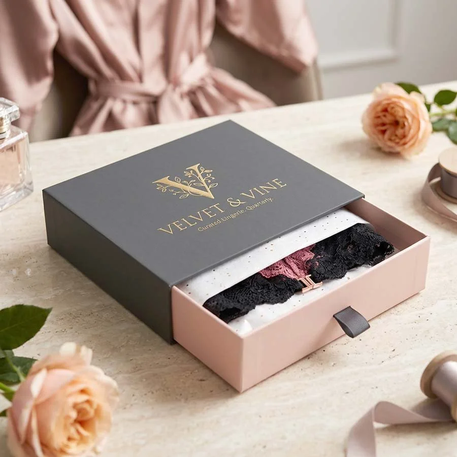 Luxury fashion packaging drawer box with foil branding, ribbon pull and precision fit insert presenting premium lingerie in a lifestyle setting
