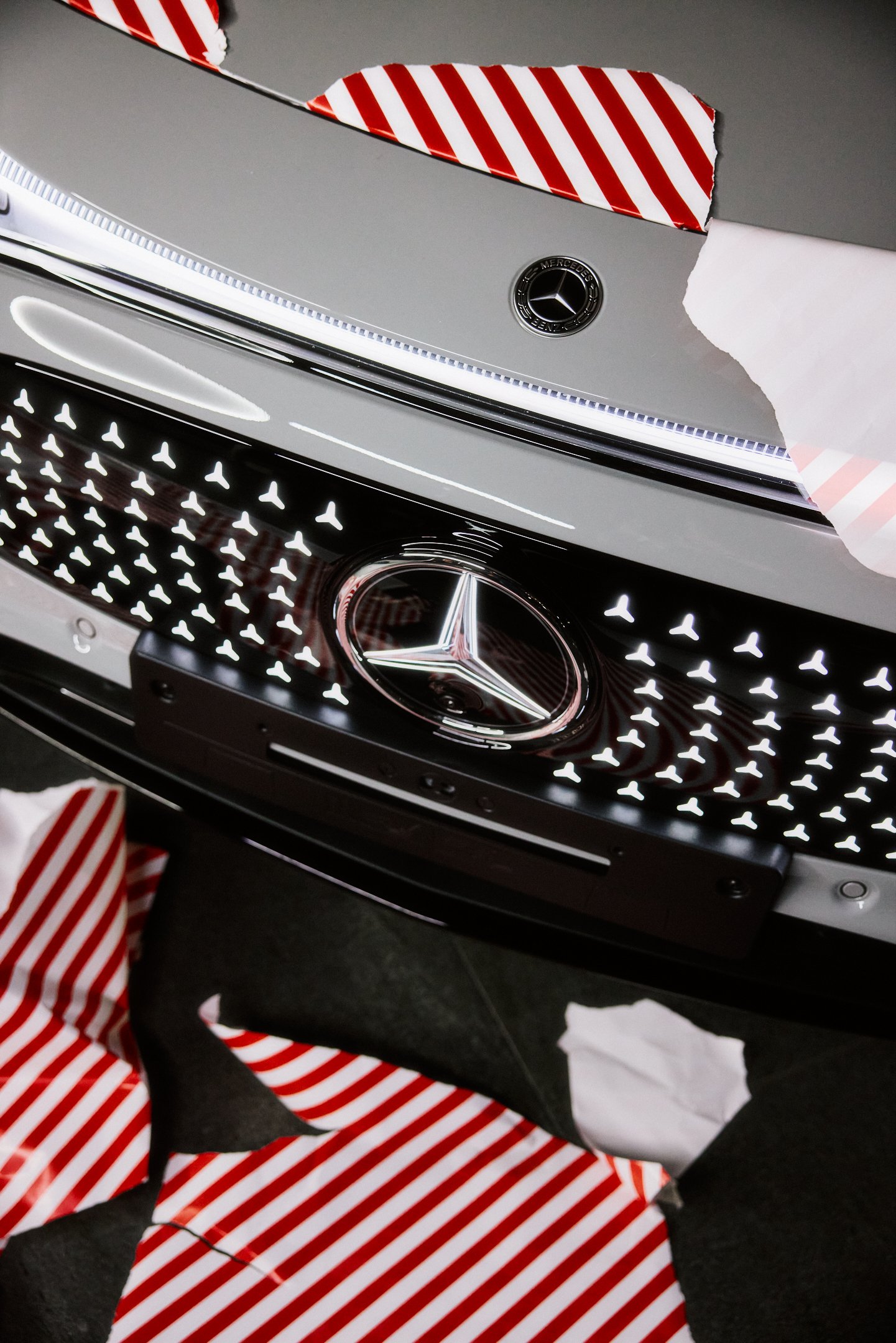 Detailaufnahme Mercedes Stern und beleuchteter Grill, grafische Strukturen mit Geschenkpapier Fragmenten.