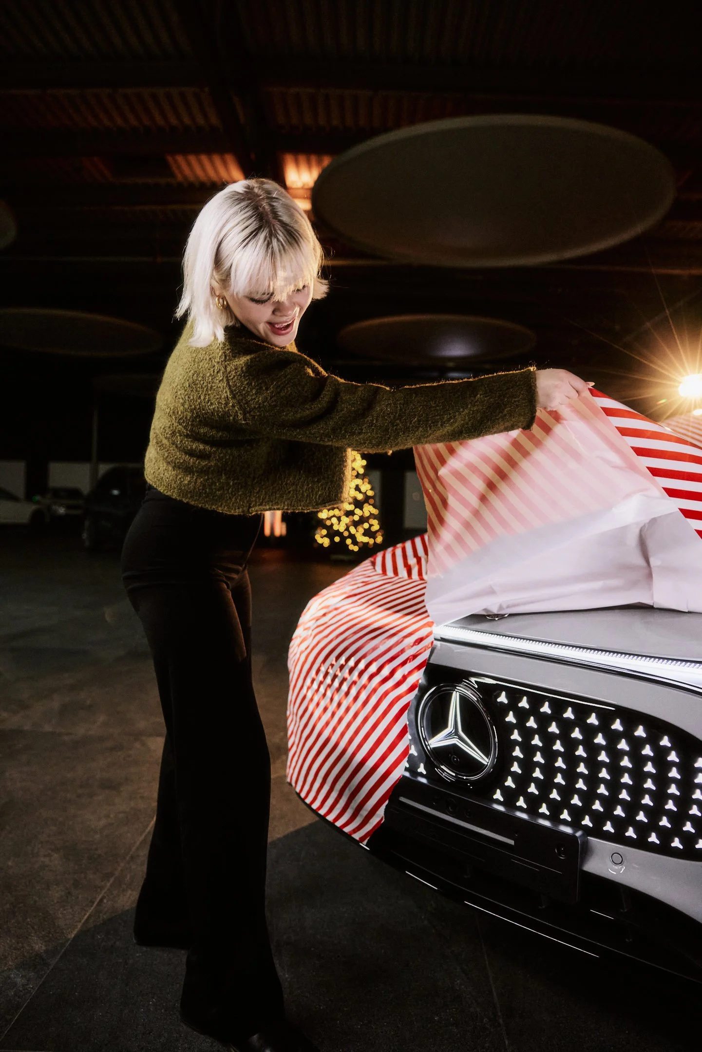 Lifestyle Motiv für Social, Person zieht Geschenkpapier von der Fahrzeugfront, Mercedes Stern im Hintergrund.