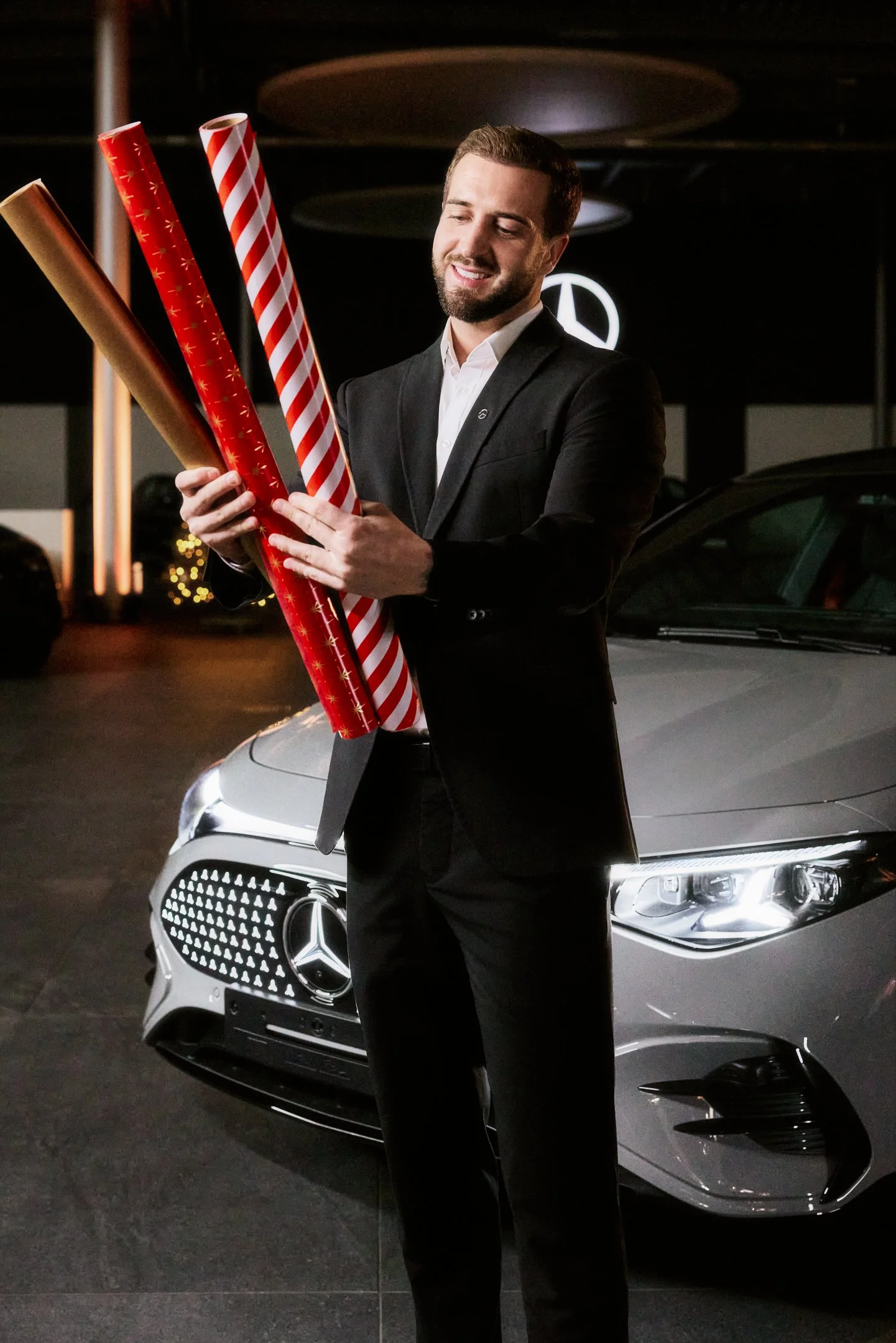 Business Portrait im Mercedes Benz Showroom, Mitarbeiter im Anzug mit Geschenkpapier Rollen vor Fahrzeug und Logo.