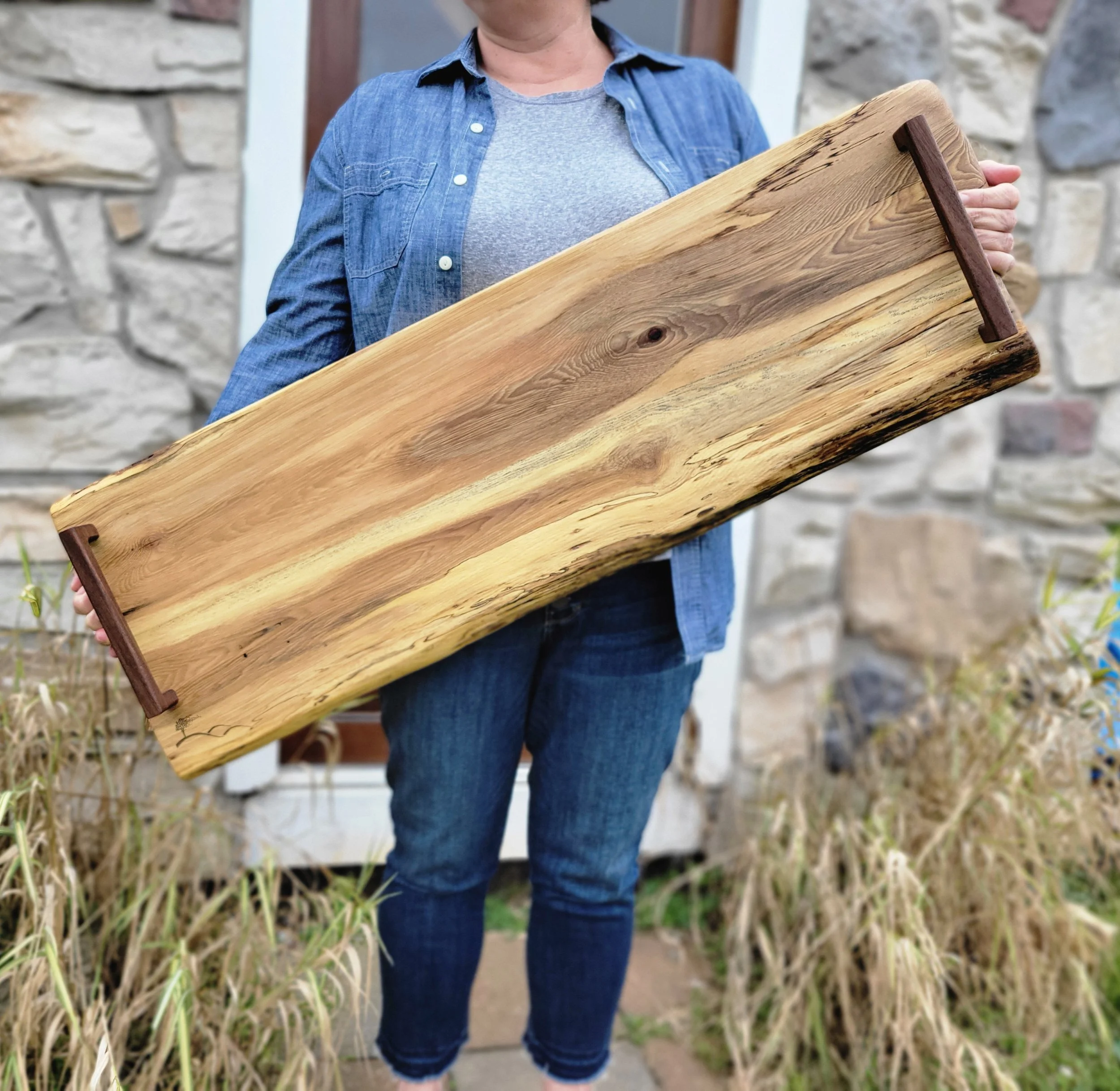 Person holding a rectangular wooden tray with natural wood grain and two dark wood handles.