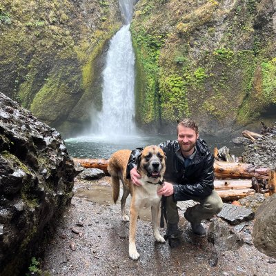 Image of employee Scott posed with a dog at his side in front of a waterfall