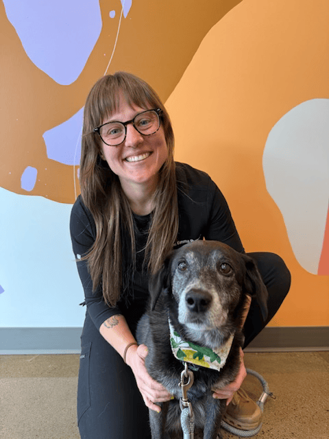 Dr Emma Rupert kneels with her old dog, smiling, in front of Sadie's vibrant mural