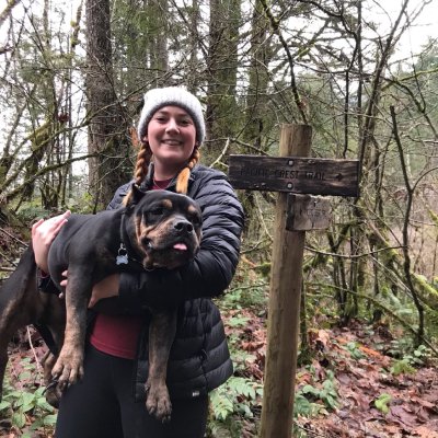 Image of employee Nikki holding her black dog in her arms while standing in nature