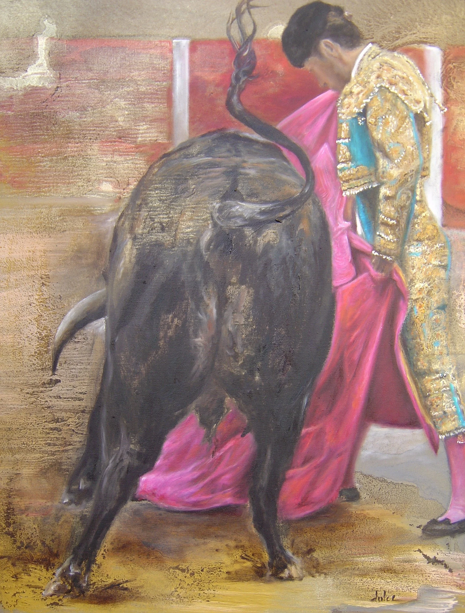 A bullfighter dressed in a traditional ornate costume stands with his back to the viewer, holding a pink cape, as a large charging bull confronts him in a bullring.