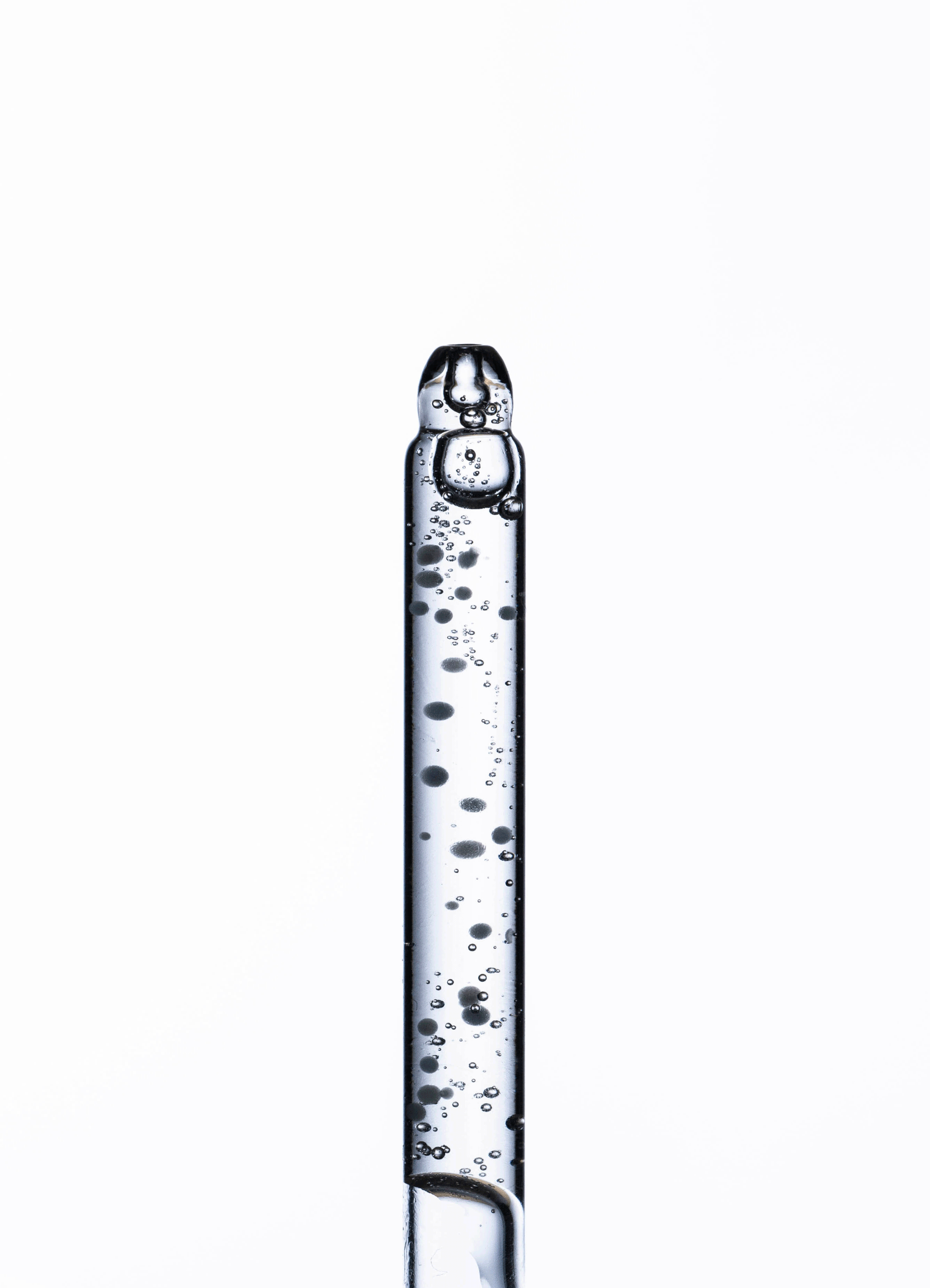 Close-up of a glass pipette with bubbles inside, standing vertically against a white background.