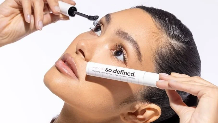A woman applying mascara to her eyelashes while holding a tube labeled 'so. defined' under her eye. Commercial Photographer Los Angeles.