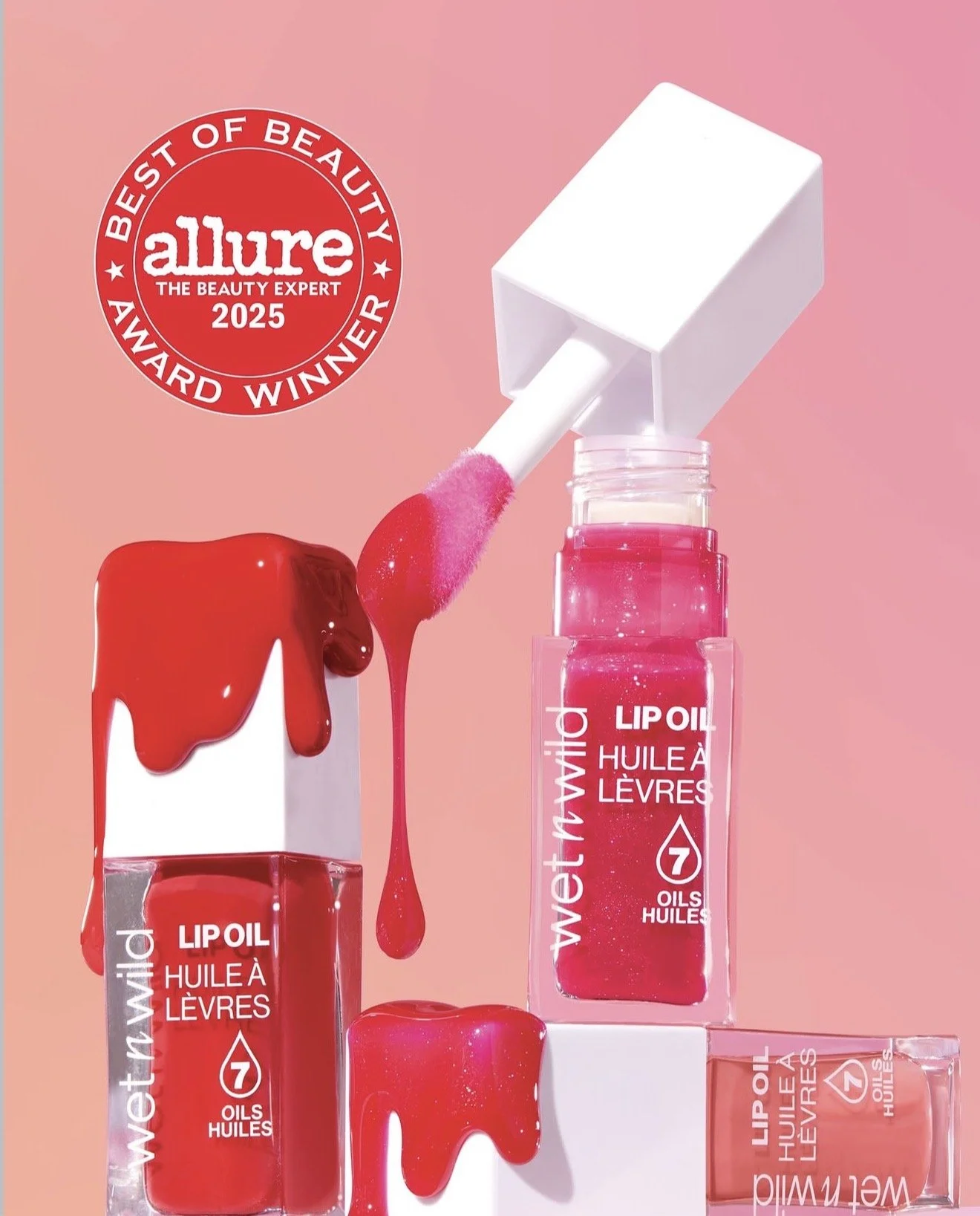 A display of three lip oil bottles in shades of red and pink with a dripping lip gloss, set against a pink background, featuring a red Allure award badge for best beauty expert 2025. Product photography Los Angeles.