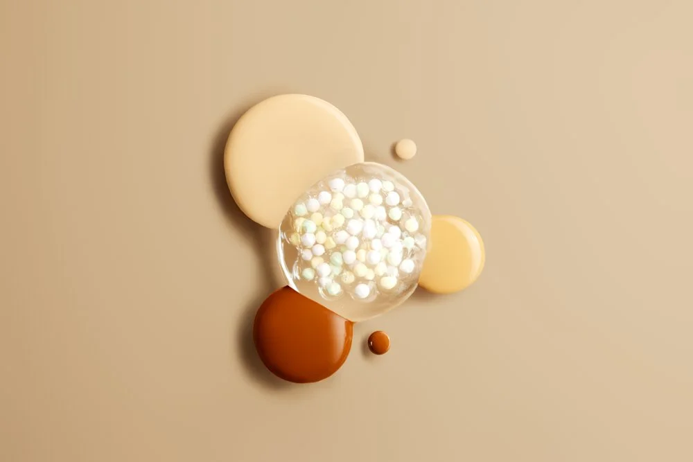 Various colored dots and spheres arranged on a beige surface, including a large transparent sphere with smaller white spheres inside, and larger beige, brown, and cream circles. Product photography Los Angeles.