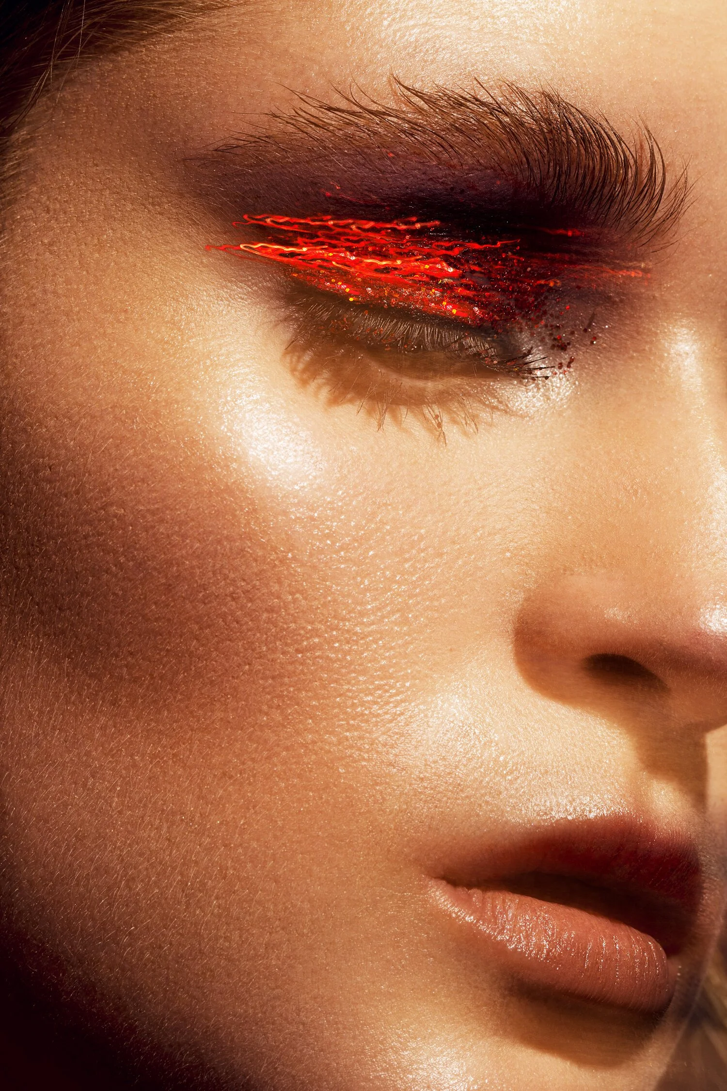 Close-up of a woman's face with eye makeup featuring red and black glitter eyeshadow. Beauty Photographer Los Angeles.