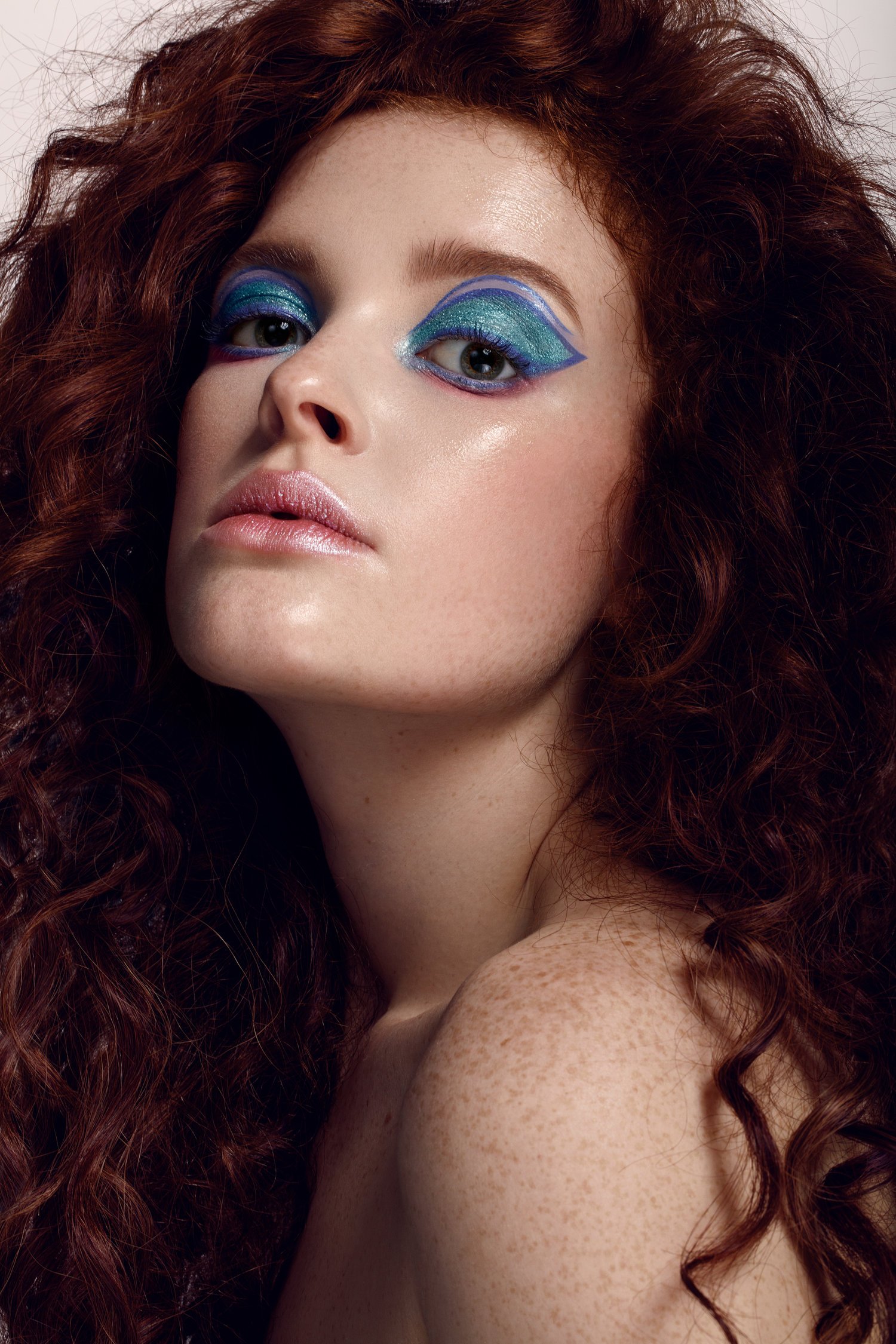 Close-up of a woman with long, curly red hair and colorful, artistic eye makeup. Beauty Photographer Los Angeles.