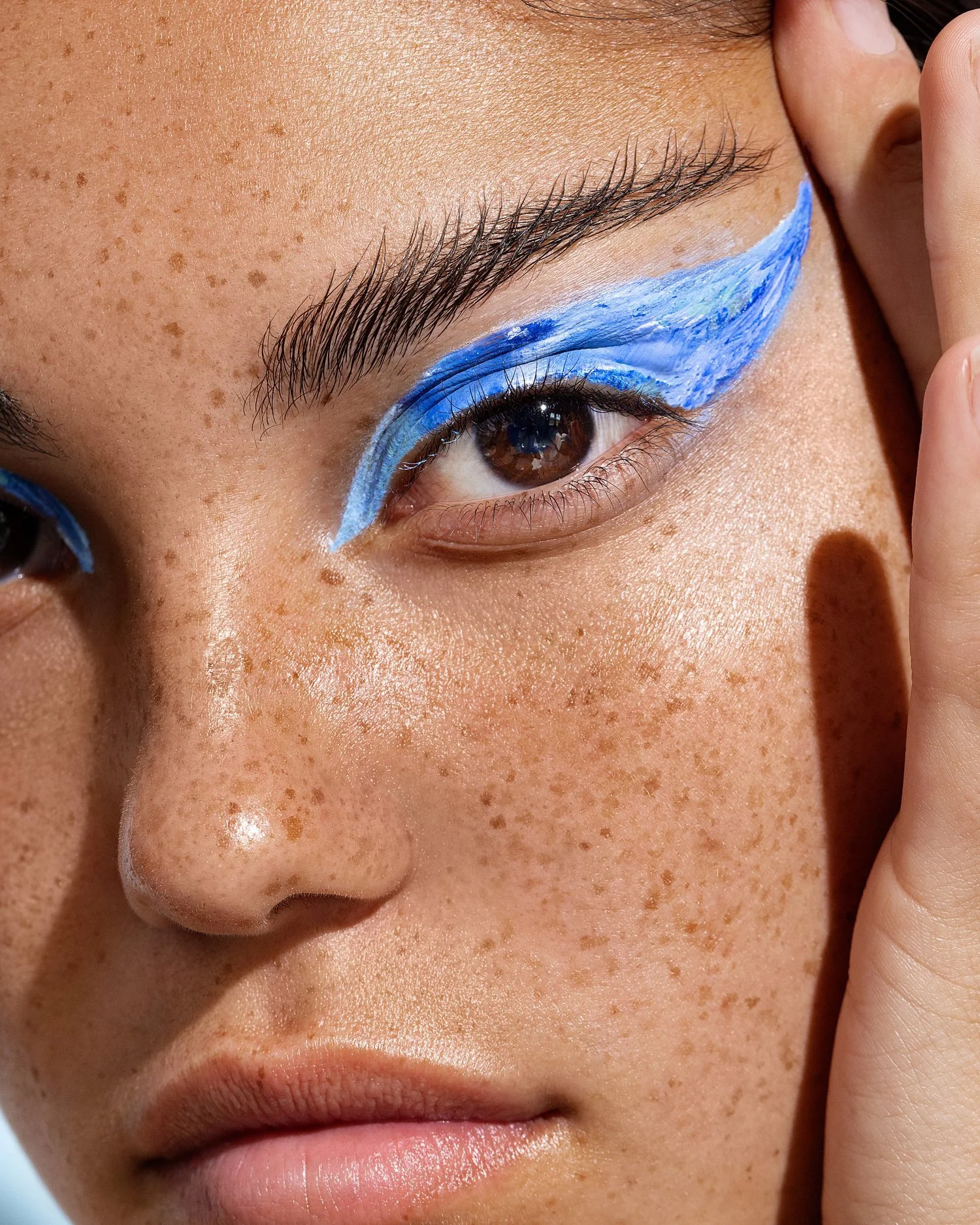 Close-up of a person's face with brown eyes, freckles, and painted blue eye makeup. Beauty Photographer Los Angeles.