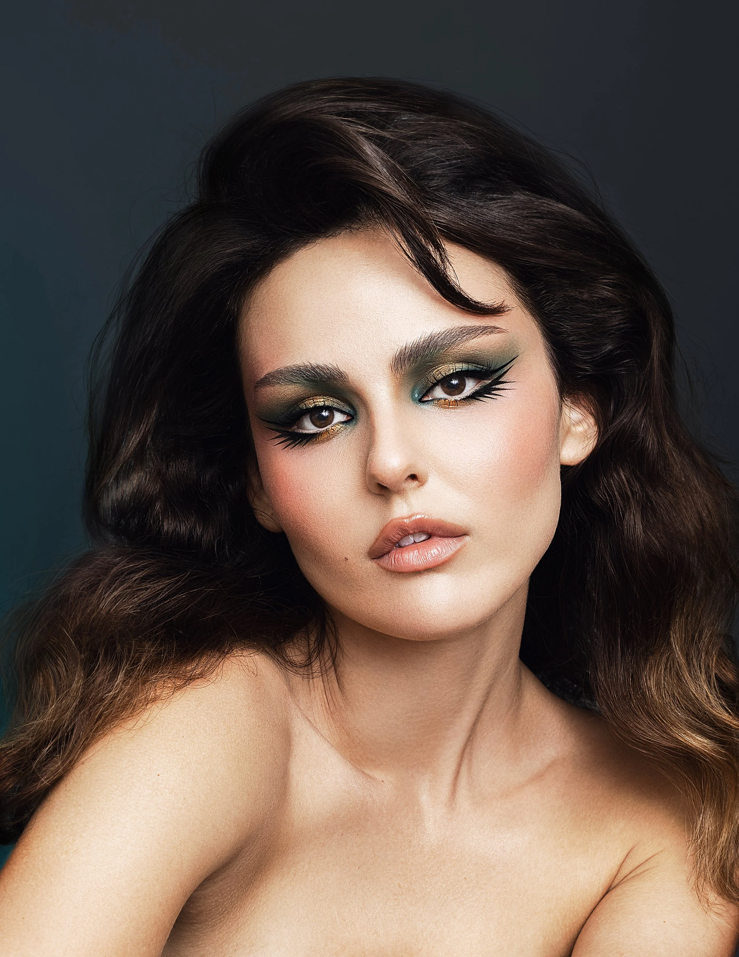 Close-up of a woman with dark brown wavy hair and dramatic makeup, including bold eyeliner, eyeshadow, and nude lipstick. Beauty Photographer Los Angeles.