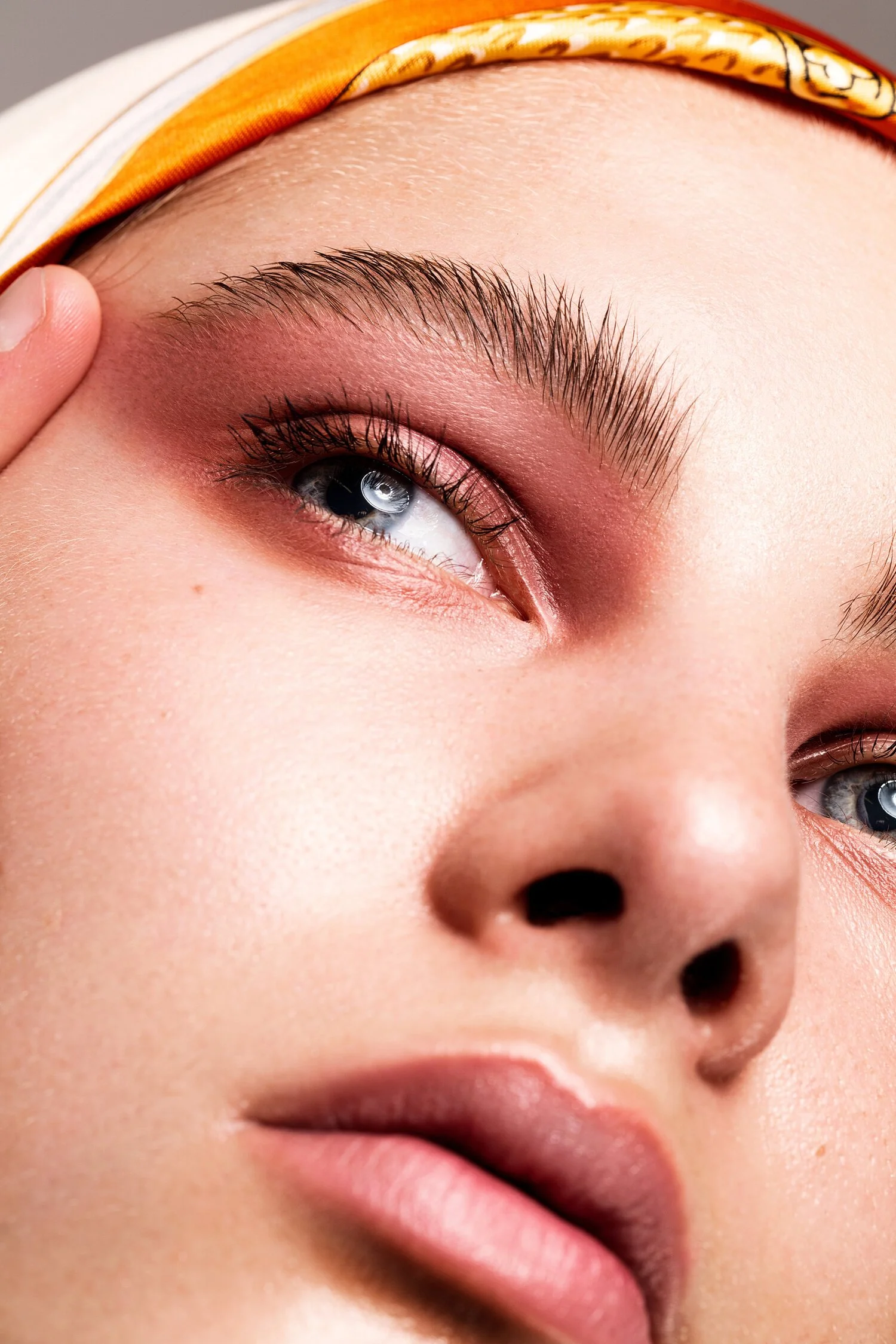 Close-up of a woman's face highlighting her blue eye, well-groomed eyebrows, and smooth skin, with a portion of her lips visible and a colorful headband. Beauty Photographer Los Angeles.