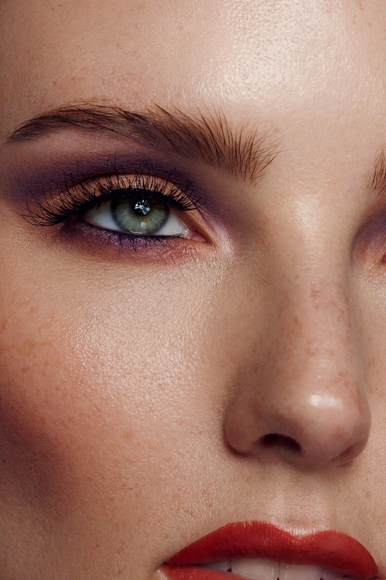 Close-up of a woman’s face showing her eye, nose, and red lips with makeup and natural skin texture. Beauty Photographer Los Angeles.