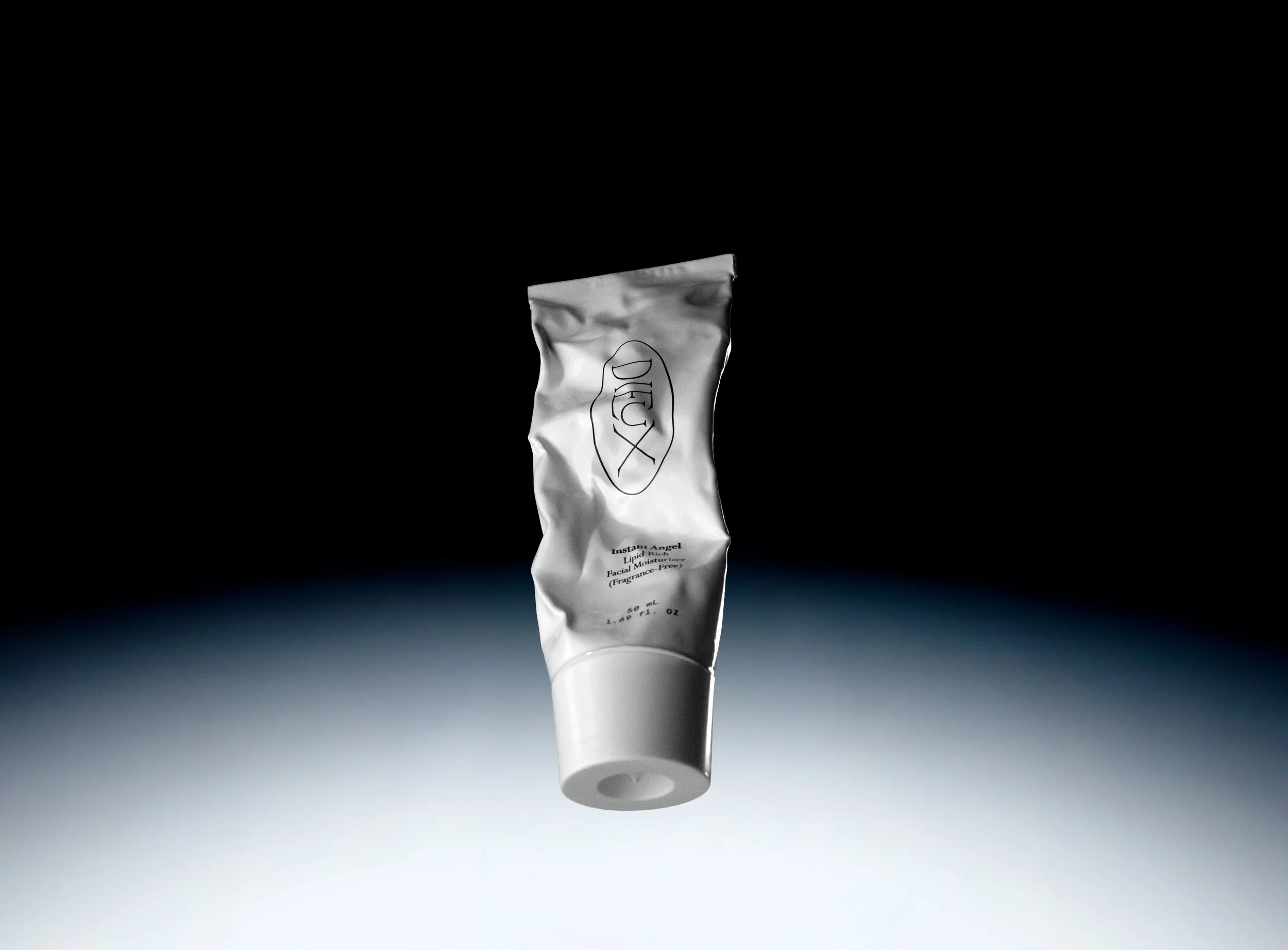 A white tube of Lipid Rich Facial Moisturizer by Drunk Elephant with black text, isolated against a dark background with a gradient, positioned upright with the cap facing down. Product photography Los Angeles.
