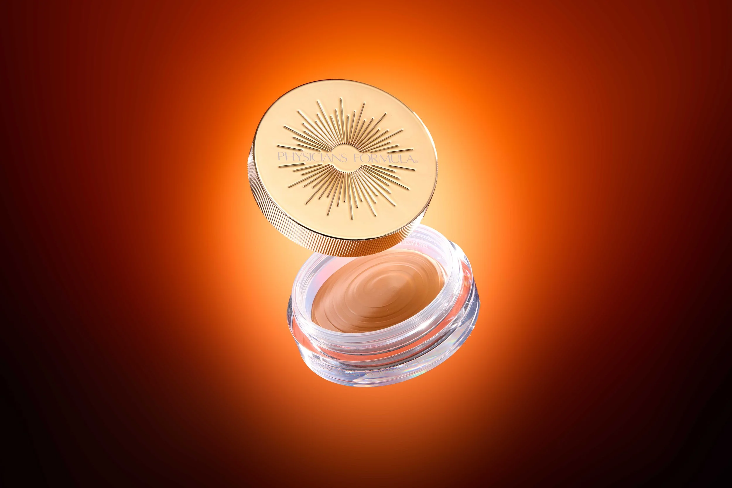 A jar of Physicians Formula foundation with the lid floating above it against a warm, glowing background. Product photography Los Angeles.