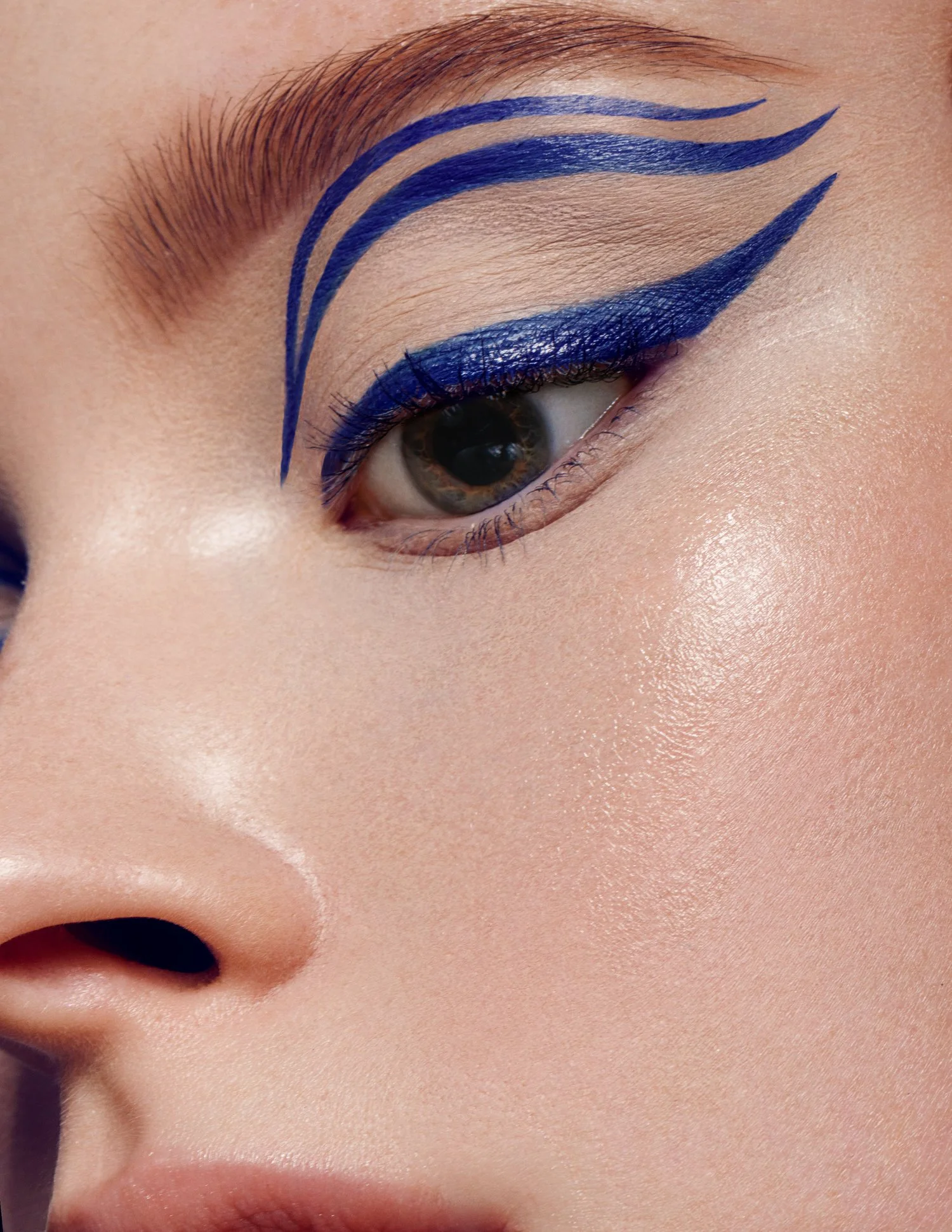 Close-up of a person's eye with artistic blue eyeliner and eyeshadow, featuring dramatic double winged lines extending from the eyelid. Beauty Photographer Los Angeles.