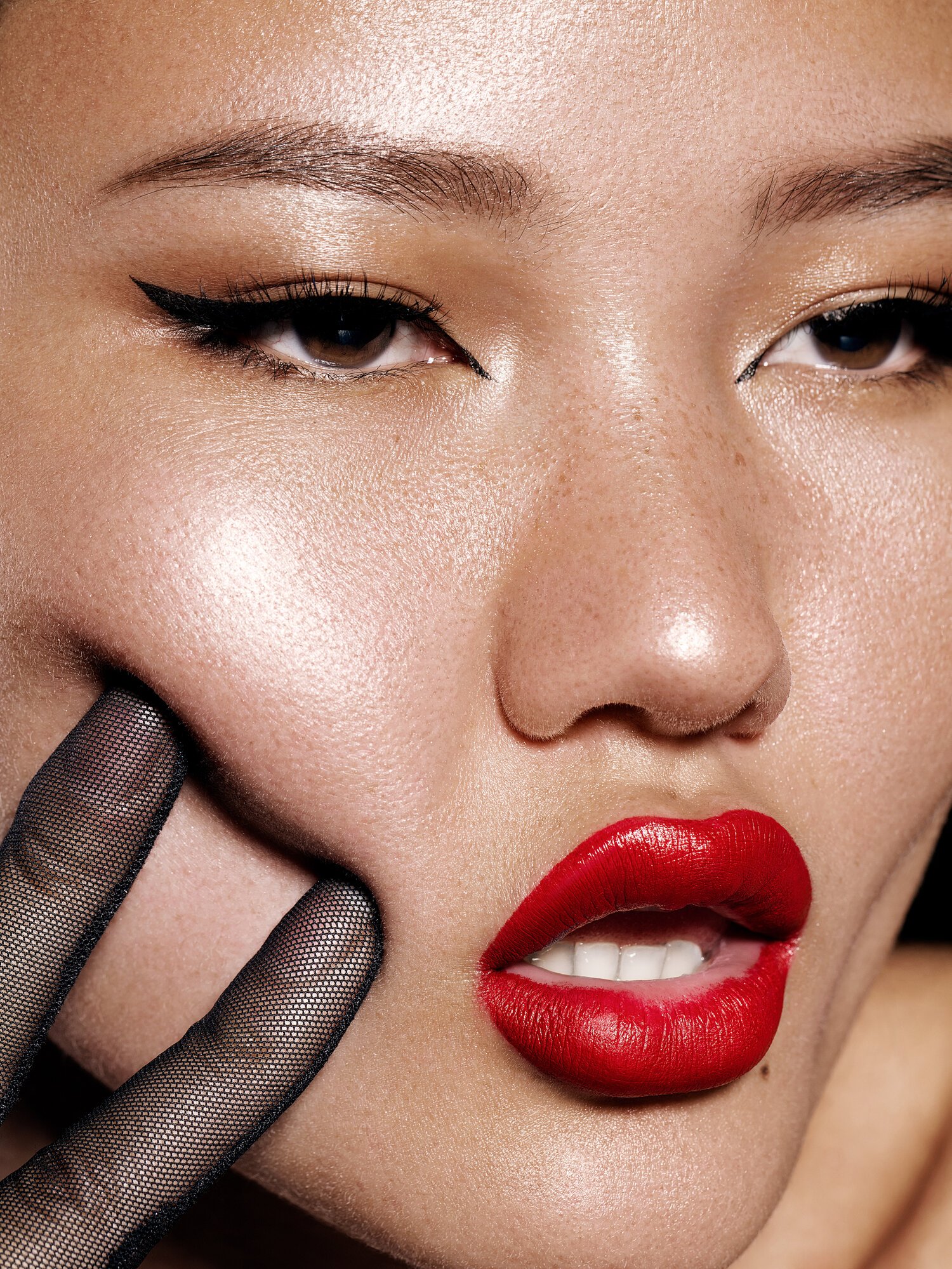 Close-up of a woman's face with bold red lipstick, winged eyeliner, and transparent gloves touching her cheek. Beauty Photographer Los Angeles.