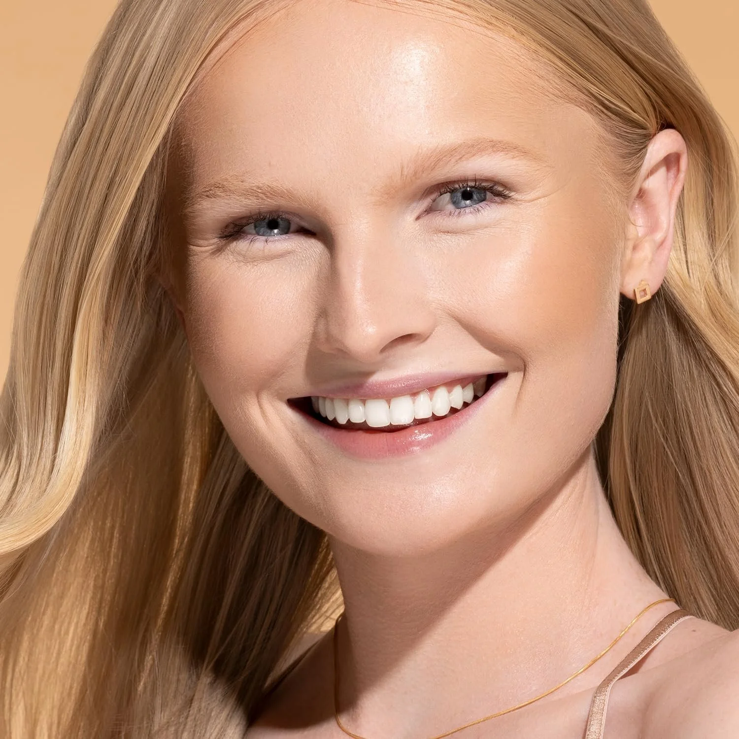 Close-up of a smiling young woman with straight blonde hair, blue eyes, and fair skin, wearing a small earring and a thin gold necklace. Commercial Photographer Los Angeles.
