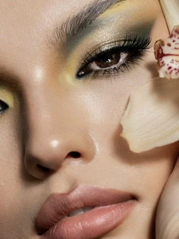Close-up of a woman with colorful eye makeup and full lips, holding a flower petal near her face. Beauty Photographer Los Angeles.