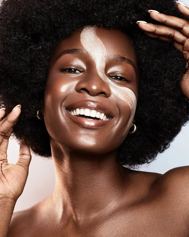 Close-up portrait of a smiling Black woman with natural curly hair, holding her hair with both hands, and face painted with white abstract lines. Beauty Photographer Los Angeles.