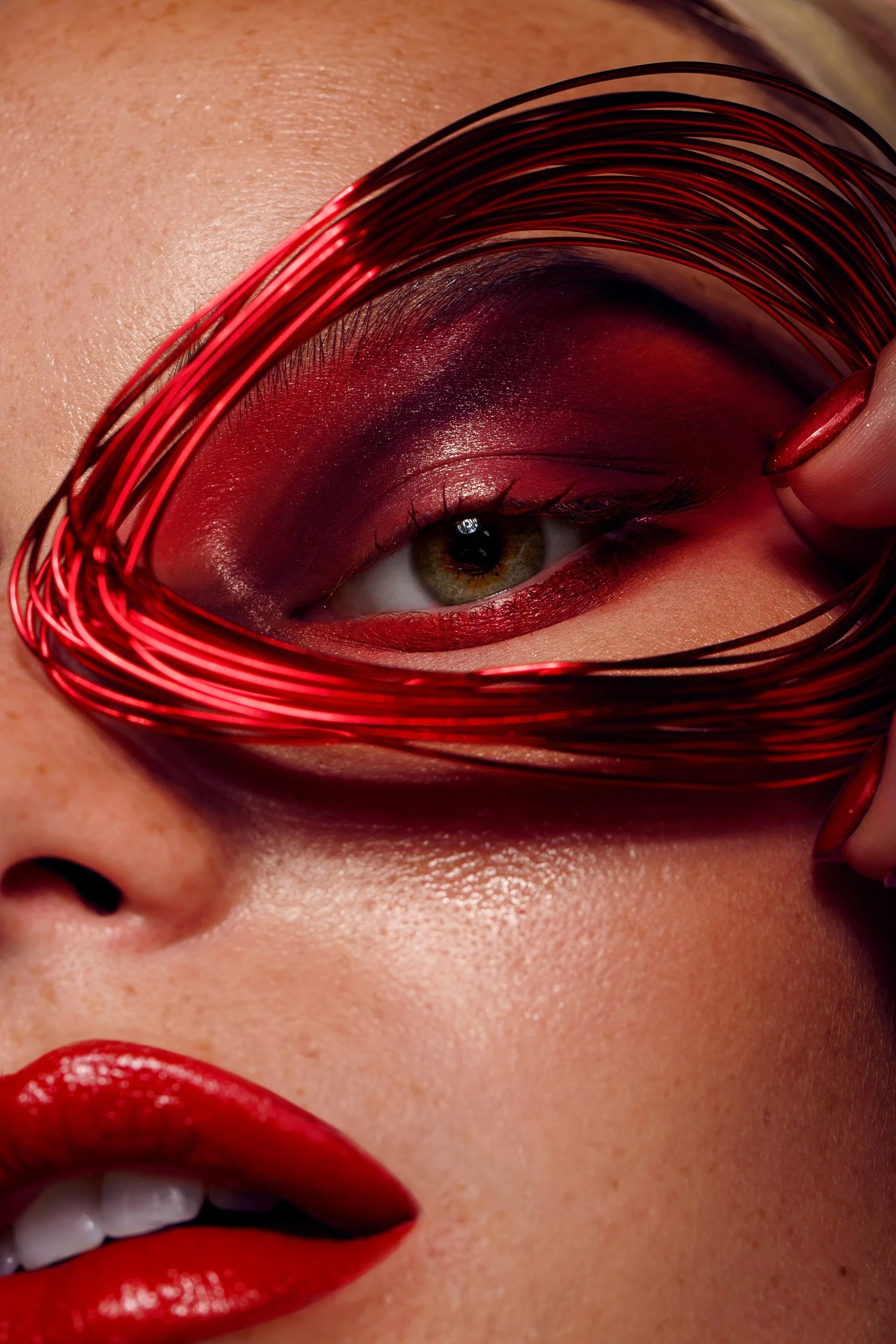 Close-up of a woman's face with red lipstick, eye makeup, and a red decorative frame around her eye, which is held up by her hand. Beauty Photographer Los Angeles.