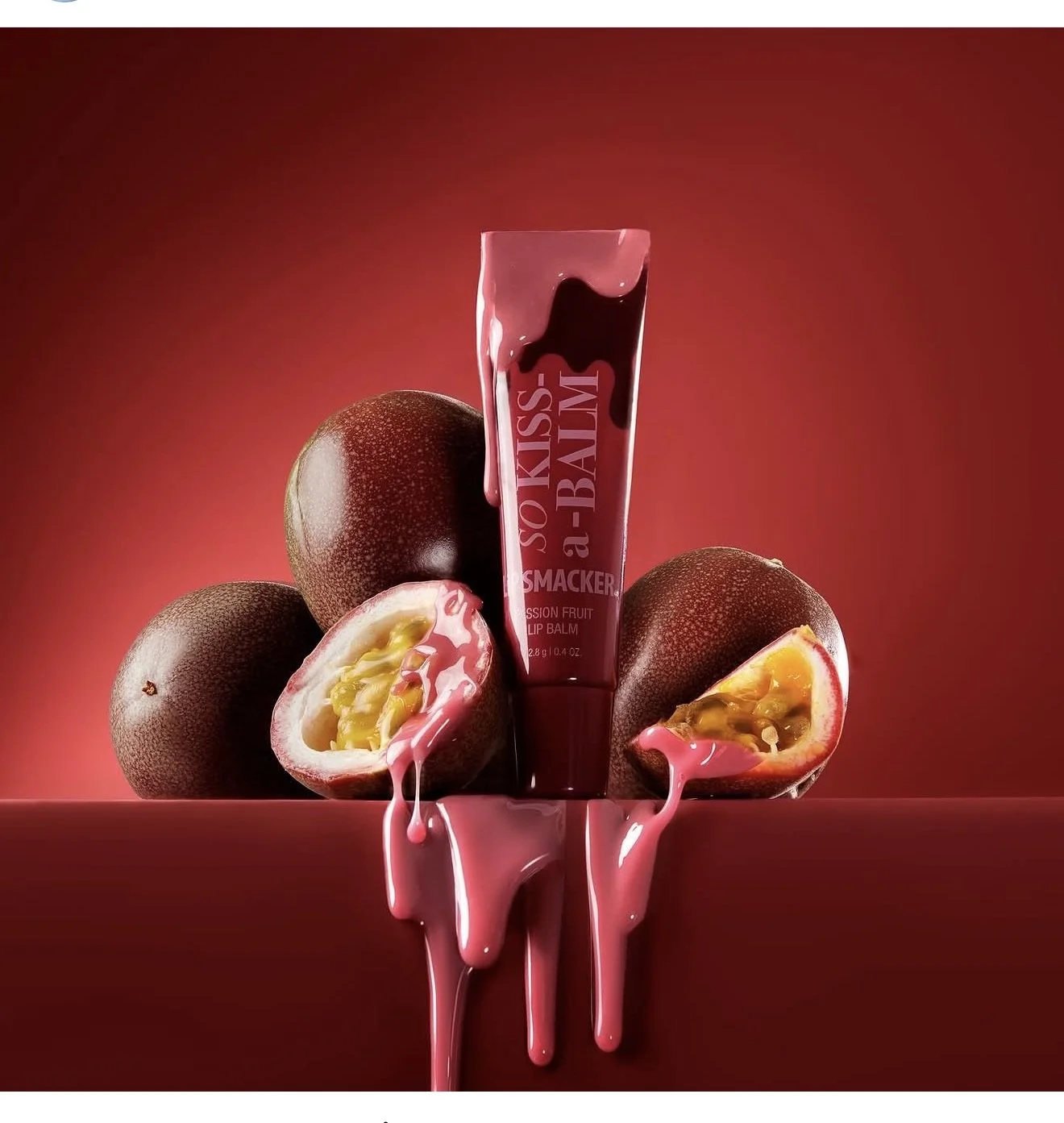 A Passion Fruit Lip Balm tube standing upright with passion fruits arranged around it, some halved revealing yellow seeds, and pink liquid spilling from the fruits and lip balm, set against a gradient red background.
