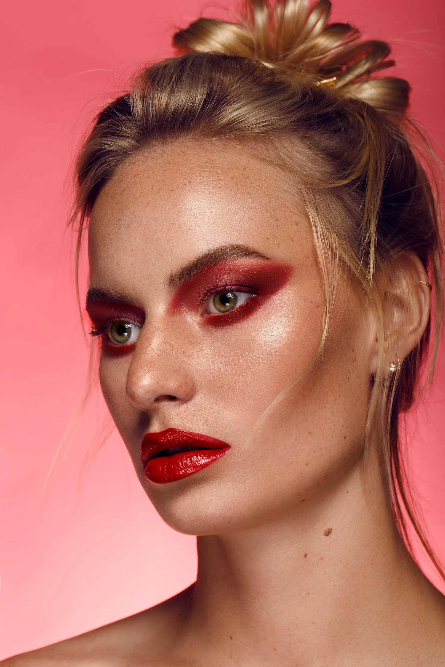 Close-up of a woman with bold red makeup, including eyeshadow and lipstick, against a pink background. Beauty Photographer Los Angeles.